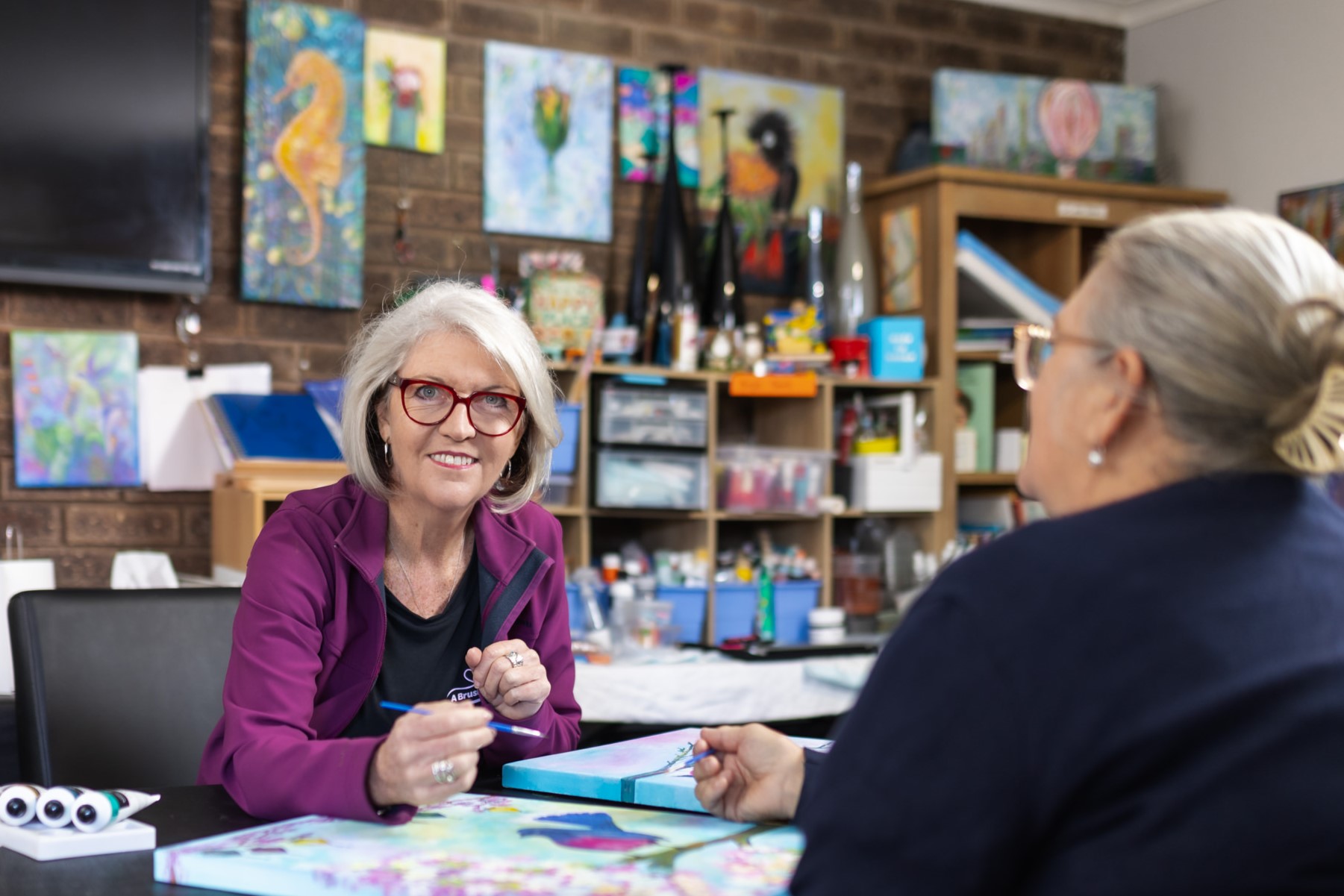 Photo of Kate Capone, owner of A Brush With Fun, sitting with a client.