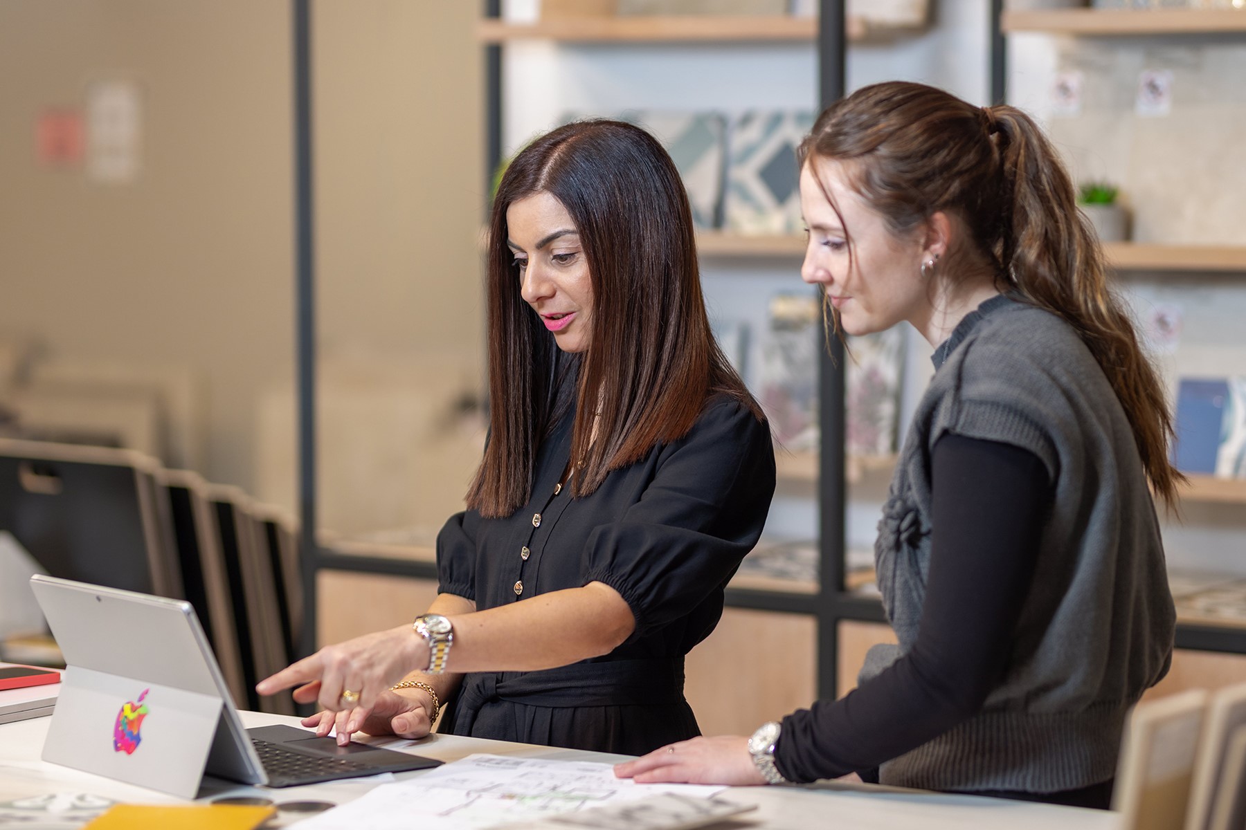 Photo of a female business owner. She is with a female customer and they are reading from a tablet device.