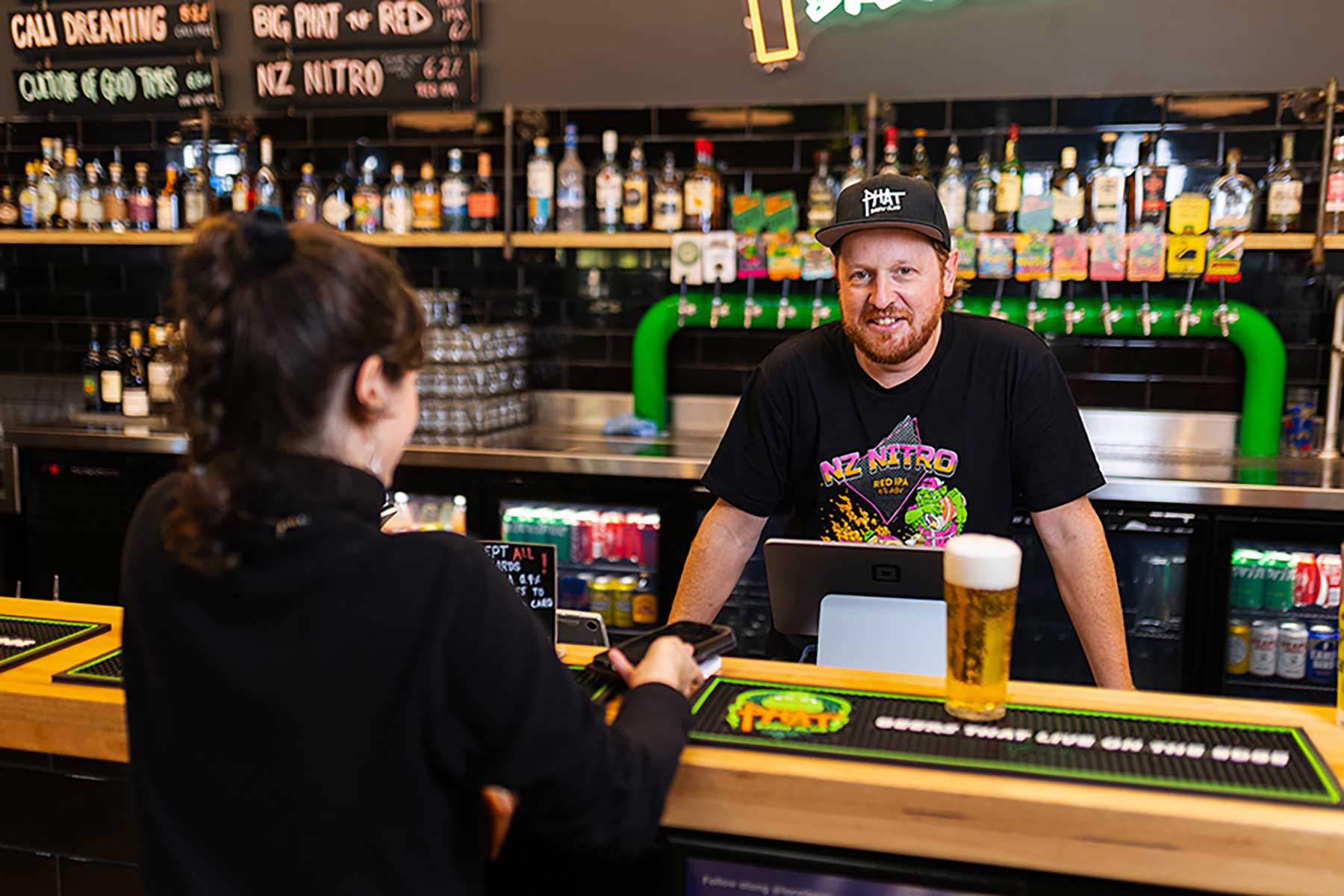 Photo of a male business owner standing behind a bar serving a customer a drink