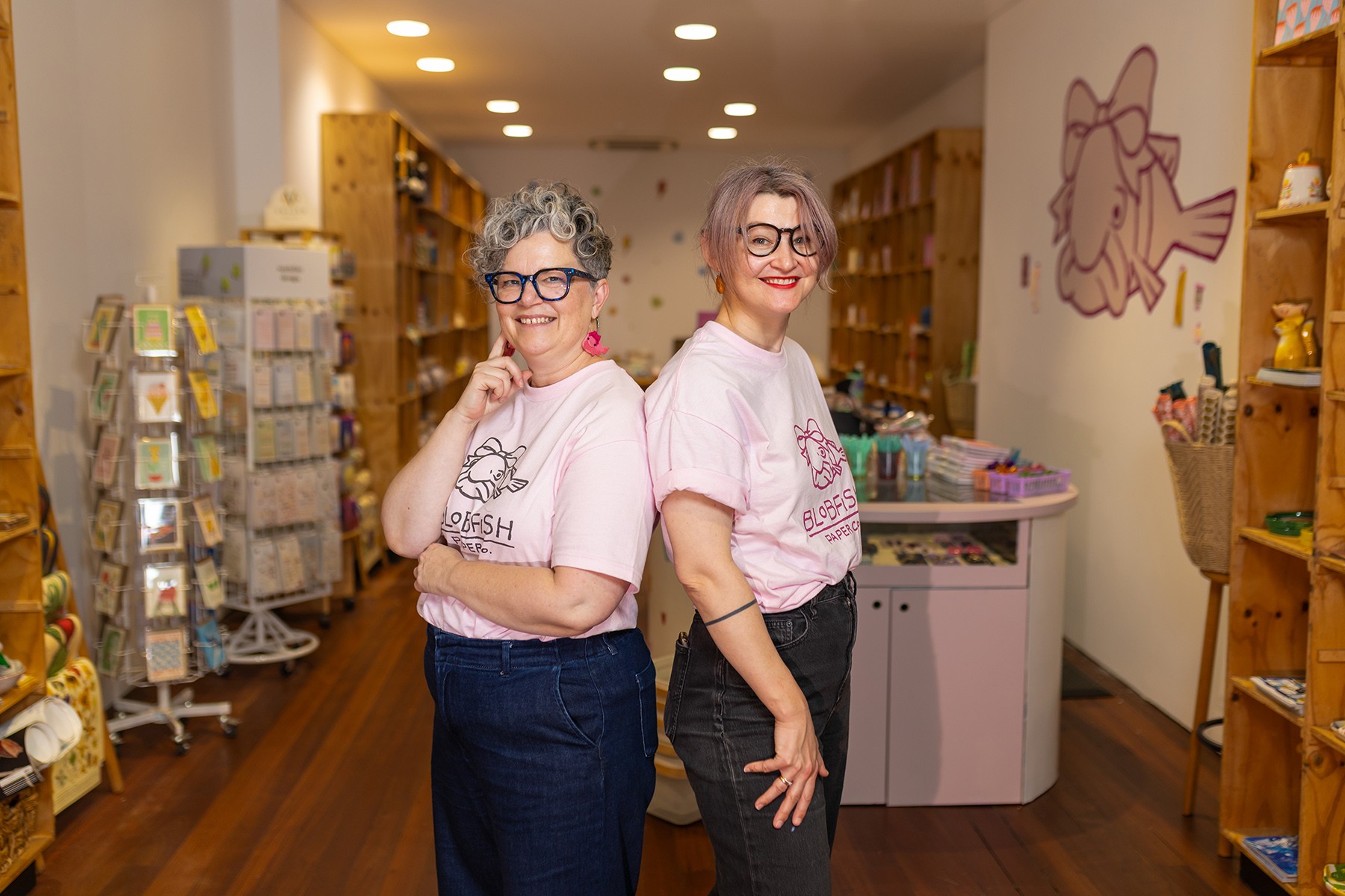 Two female business owners standing back to back in their business premises.