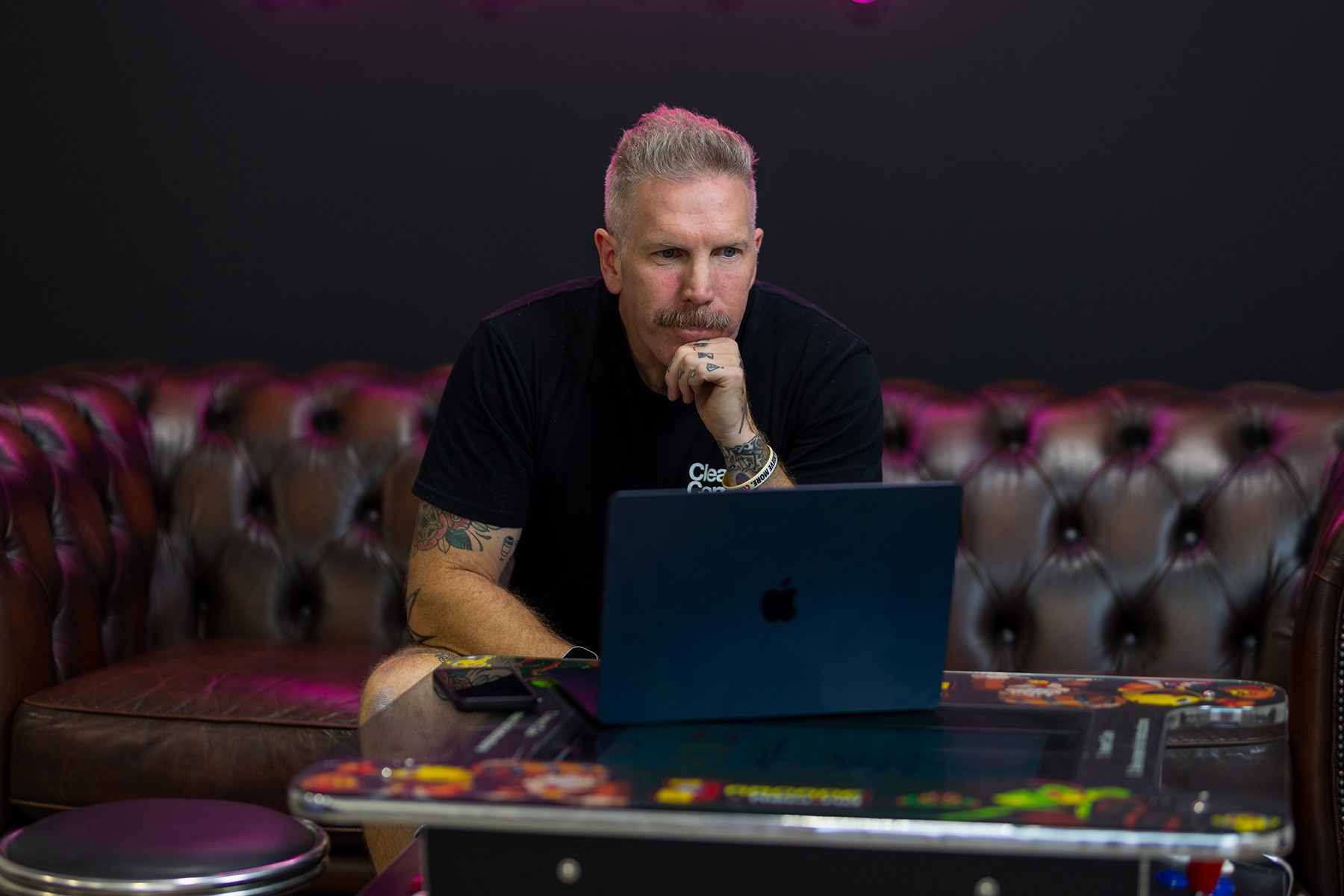 A man sitting on a couch. He is reading from a laptop.