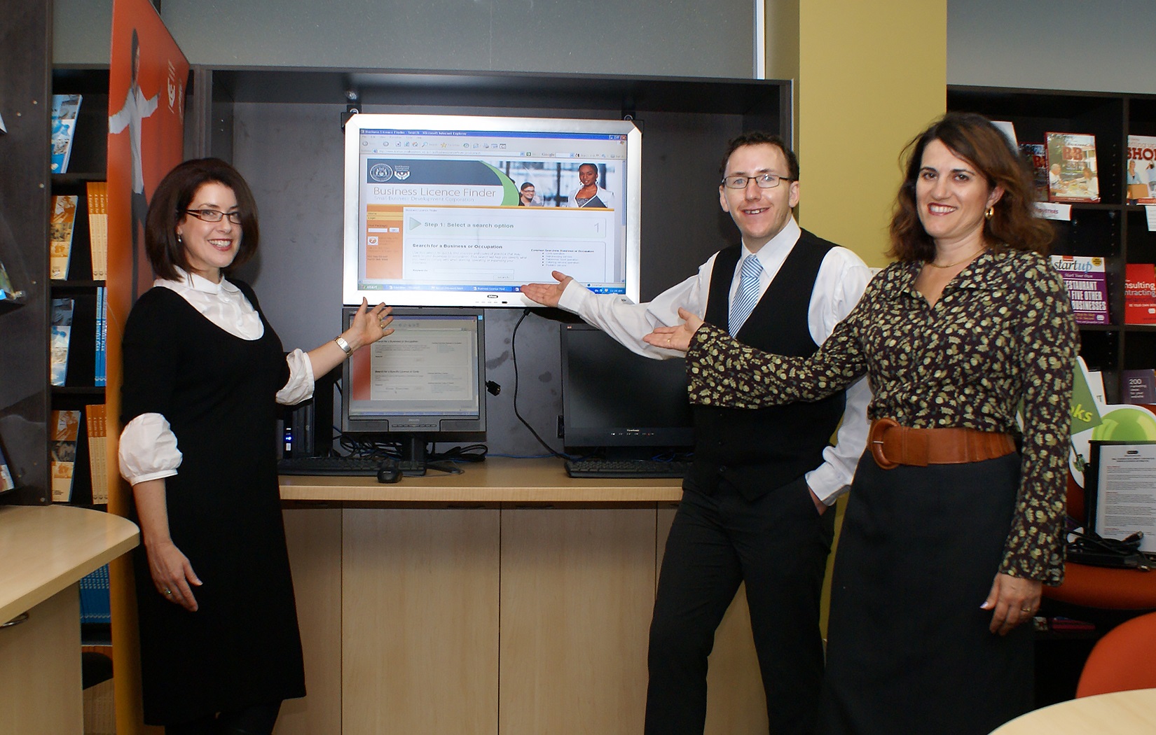 Photo of SBDC staff pointing to a large screen displaying the SBDC's newly launched Business Licence Finder website.