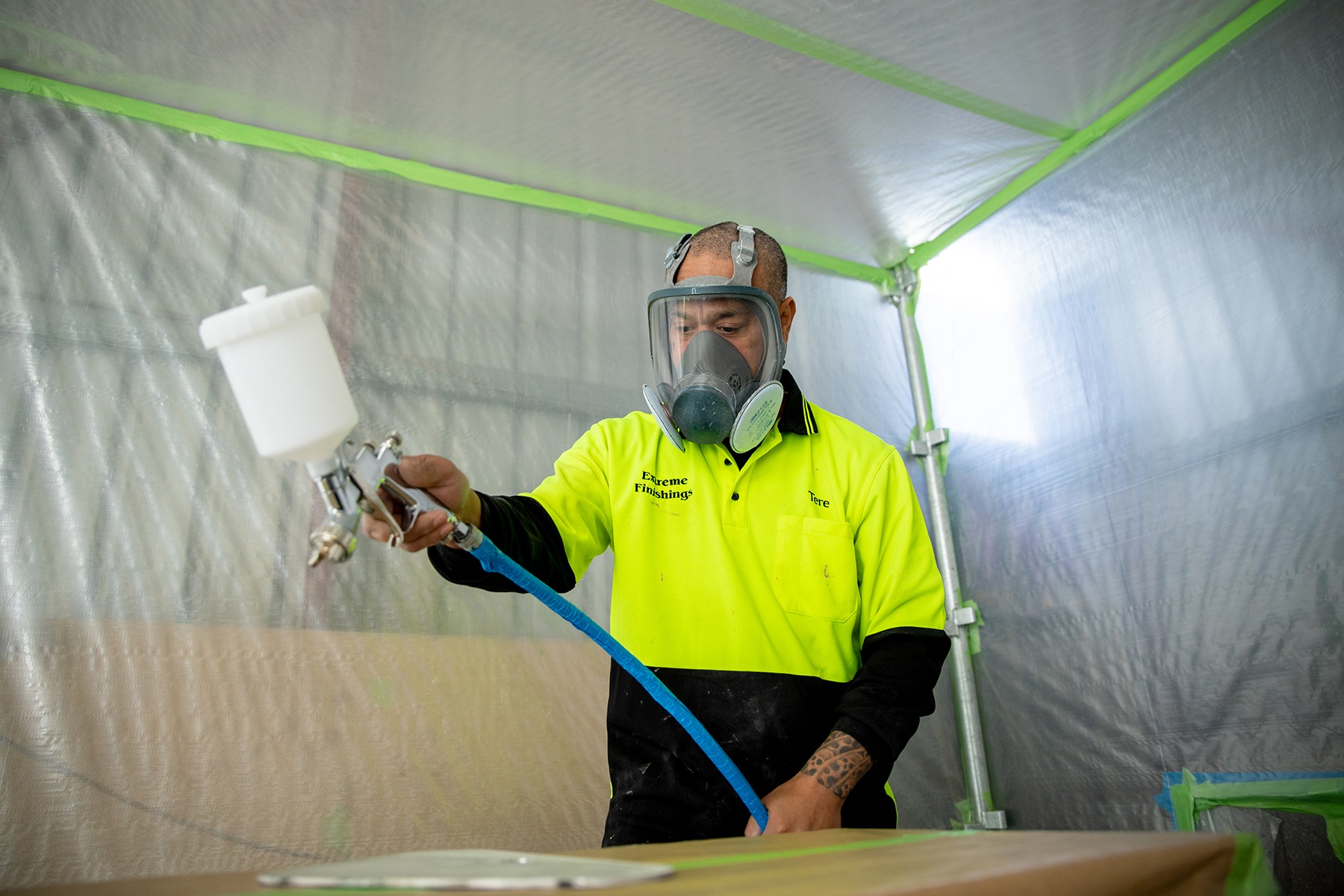 A photo of a male business owner. He is spray painting part of a boat and wearing personal protective equipment such as a face mask.