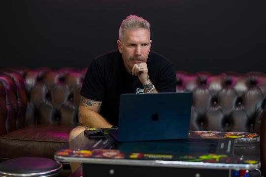 A man sitting on a couch, reading from a laptop.