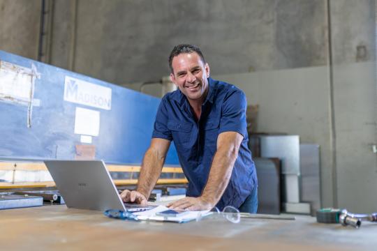 Photo of Ben Kraucevs, owner of Matrix Bore Covers. He is standing in his business premises, in front of a laptop. 