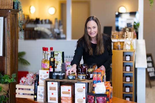 Photo of Rom Blount, owner of The Collie Providore, standing behind a display of food products in her business.