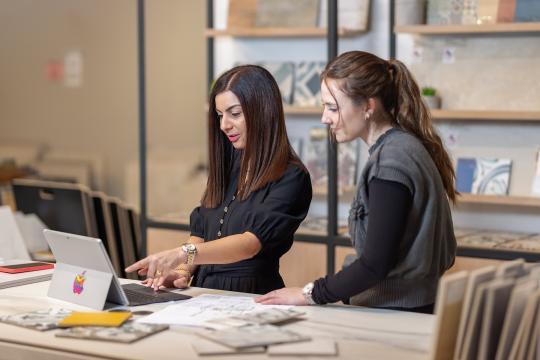 Two women looking at a laptop screen. They are standing in the retail space of a ceramics business.