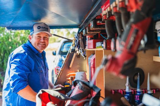 A man standing in front of a range of tools in his work van.