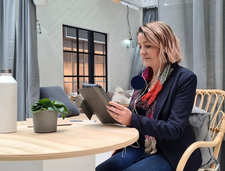 Photo of a woman sitting at a table. She is watching an SBDC workshop on a tablet device.