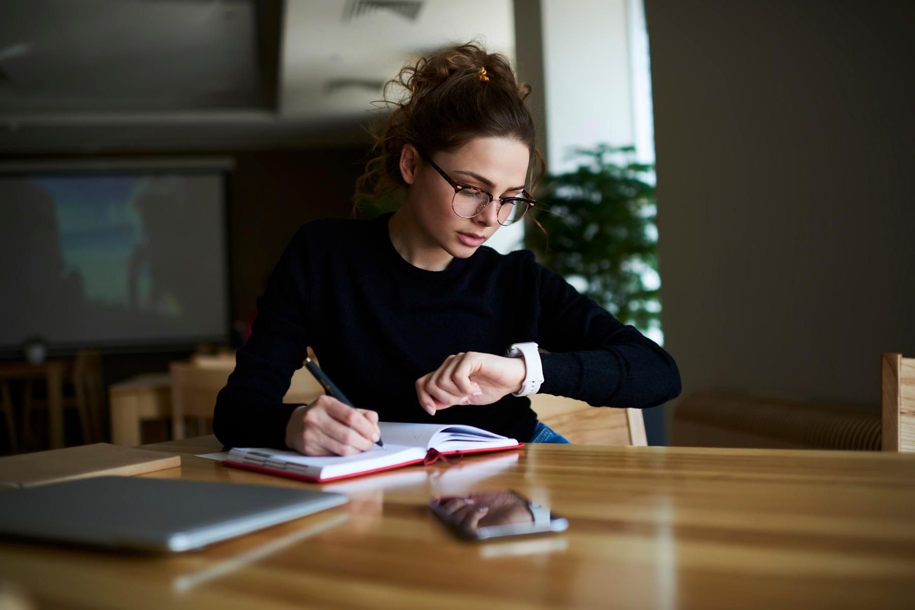 A photo of a women checking her watch while she works at a desk.