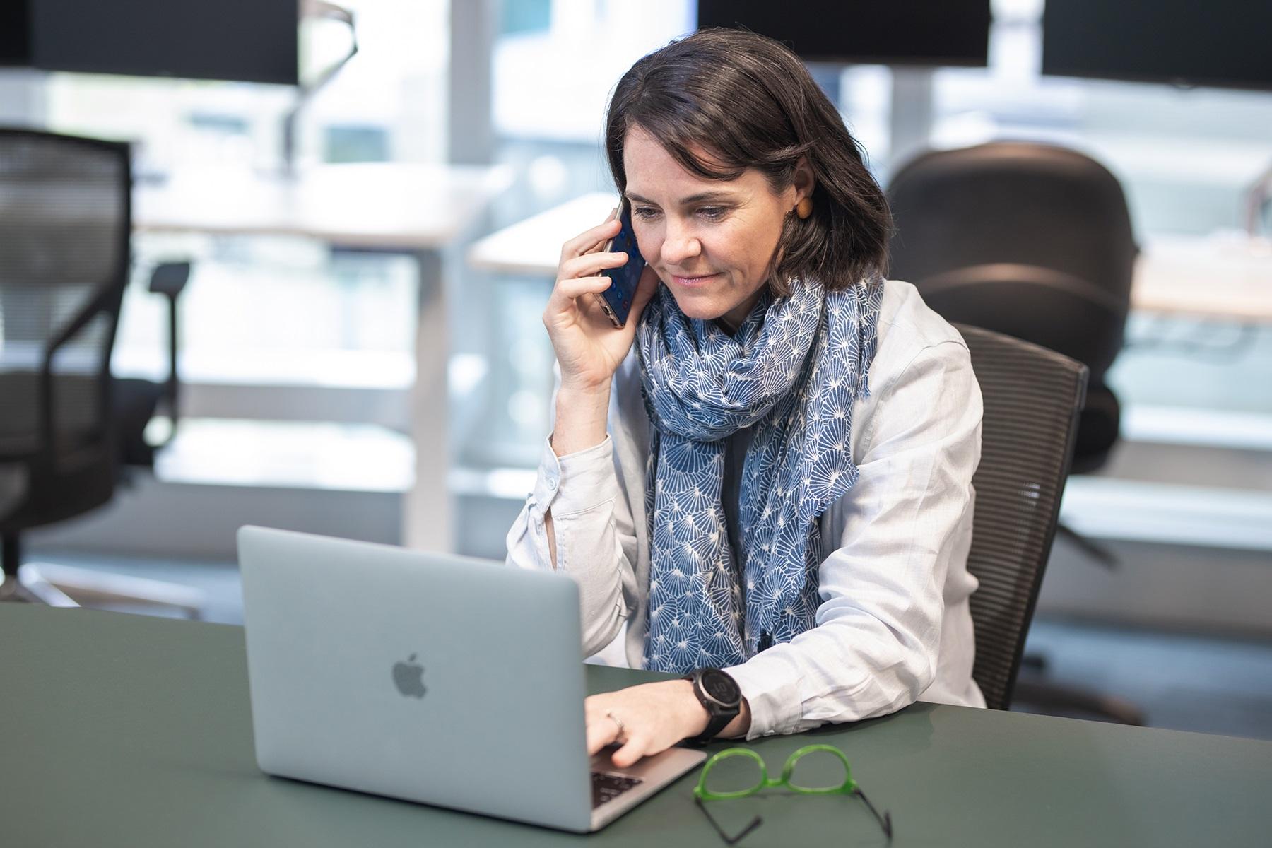 Photo of a woman working on a laptop. She is on the phone to an SBDC business adviser.