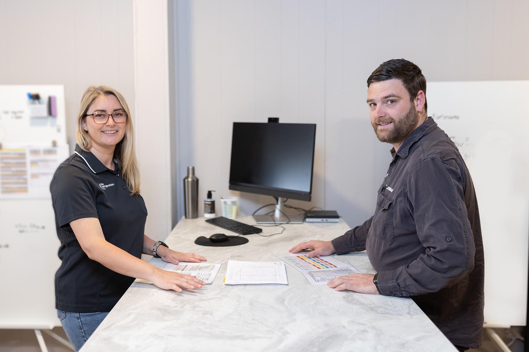 Photo of a male and female business owner standing at a work bench. 