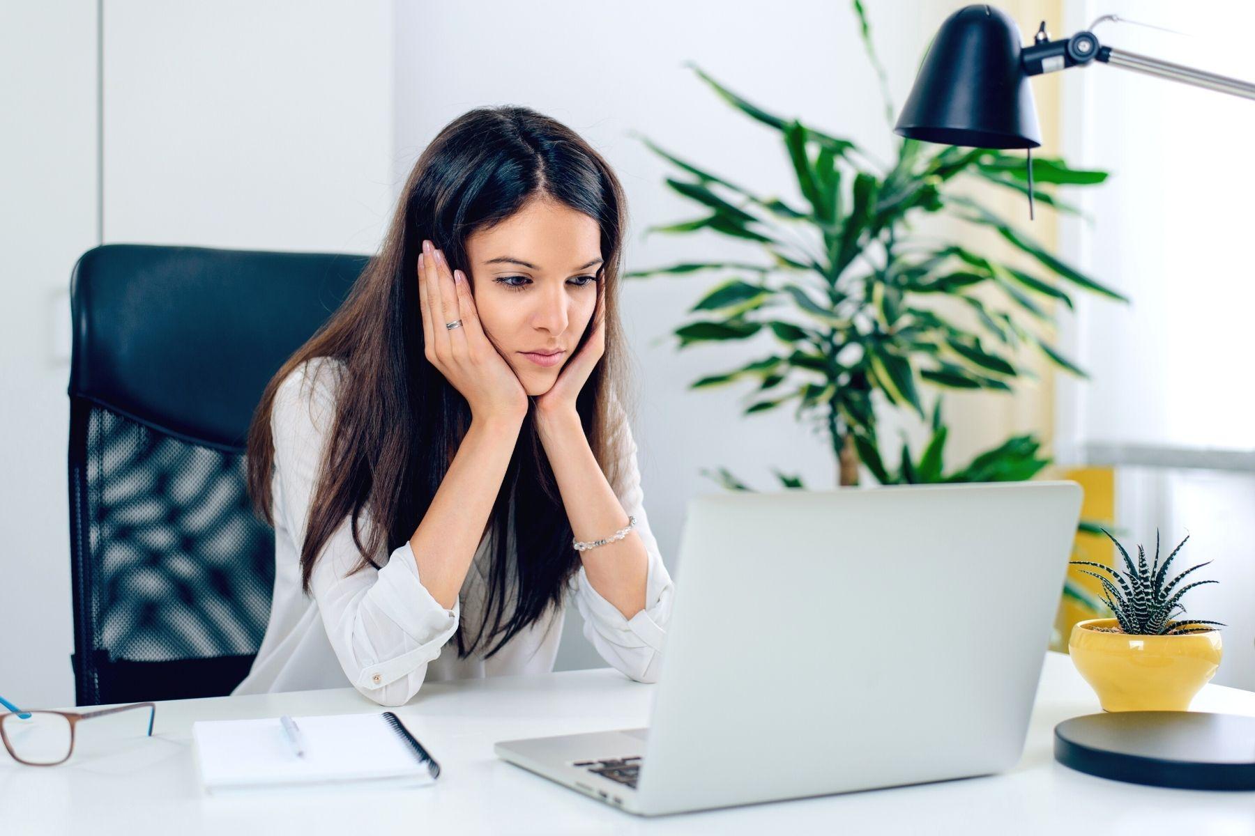Photo of a woman working in front of a laptop and looking frustrated.