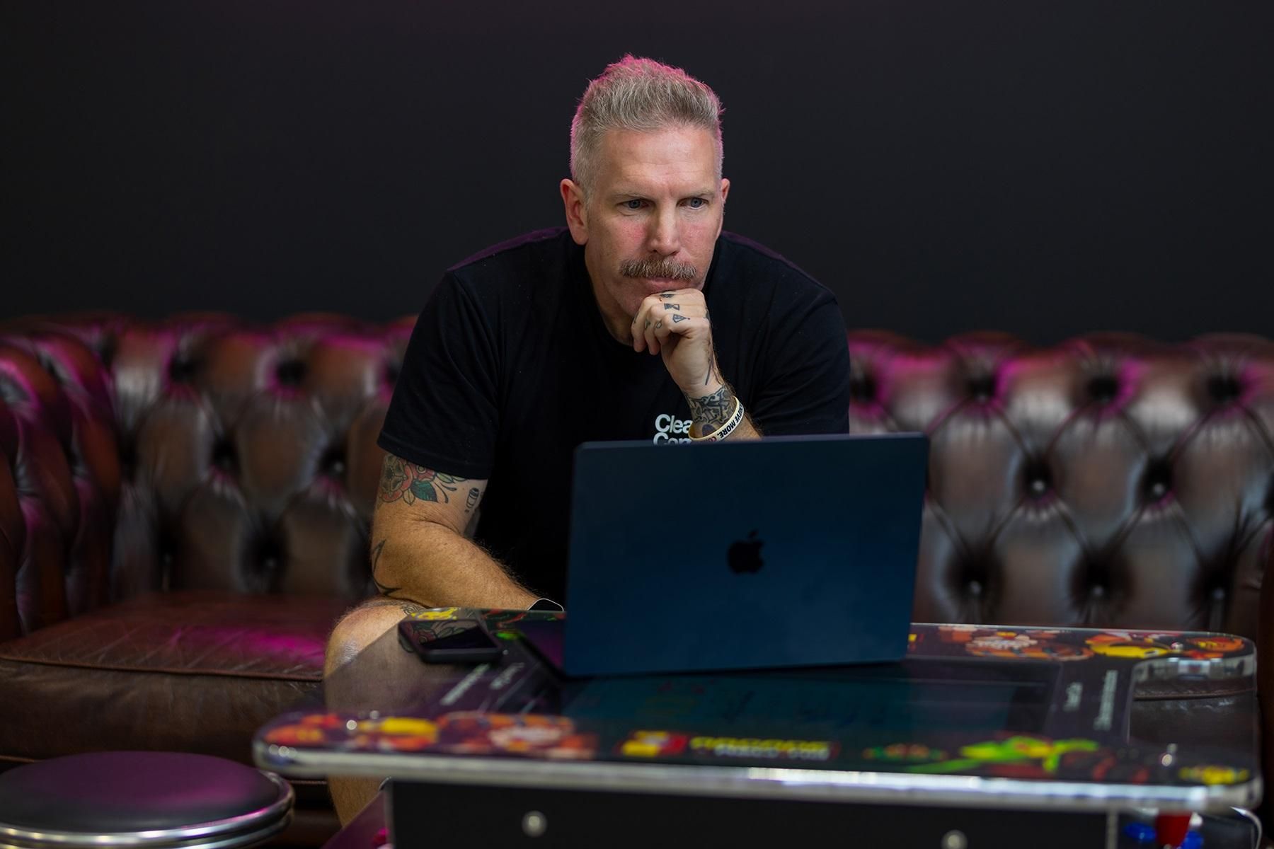 A man sitting on a couch. He is reading information on the screen of his laptop.