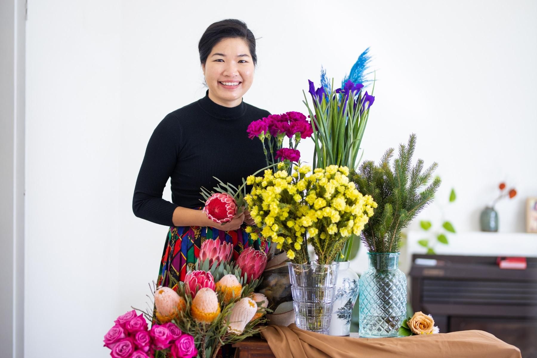 Photo of  a woman in a bridal business with vases of flowers in-front of her.