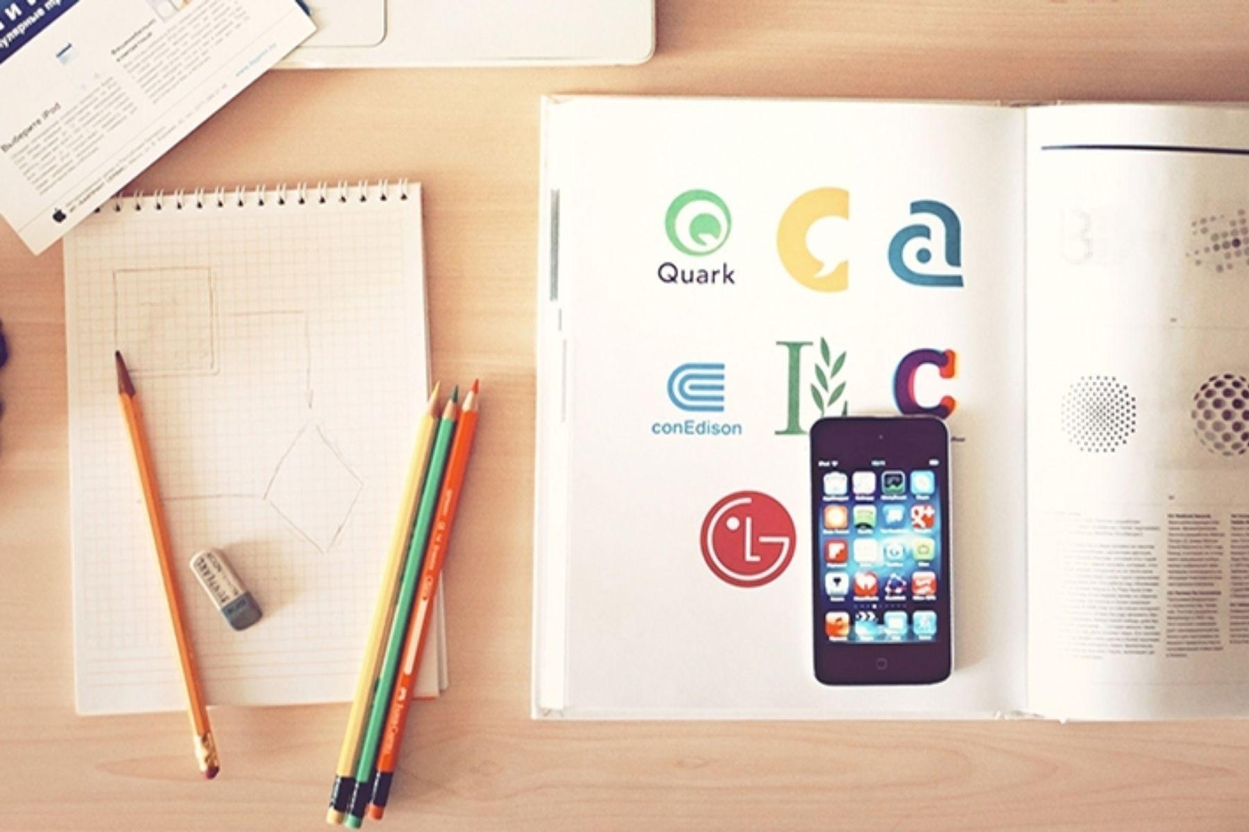 Photo of a desk with a smartphone, notebook and pencils on it.