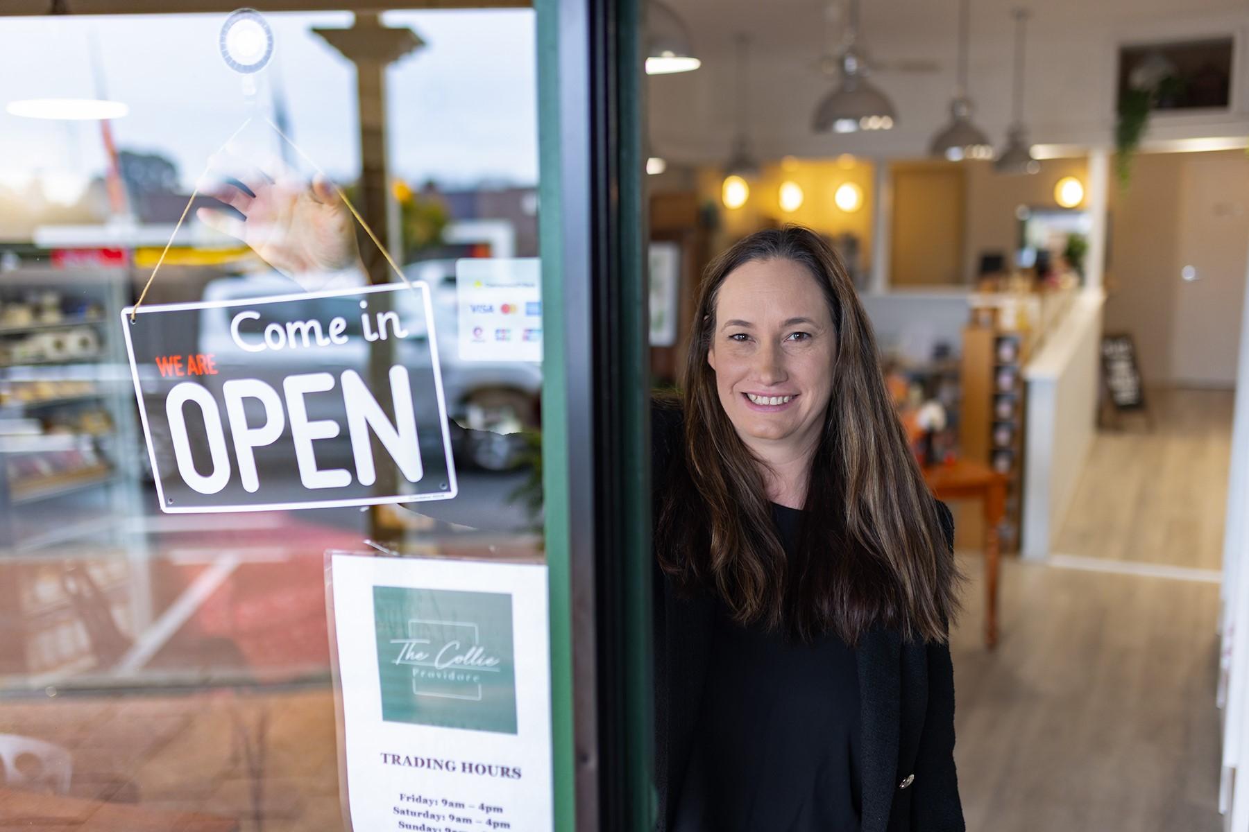 A woman standing in the entrance of her business next to an "open" sign.