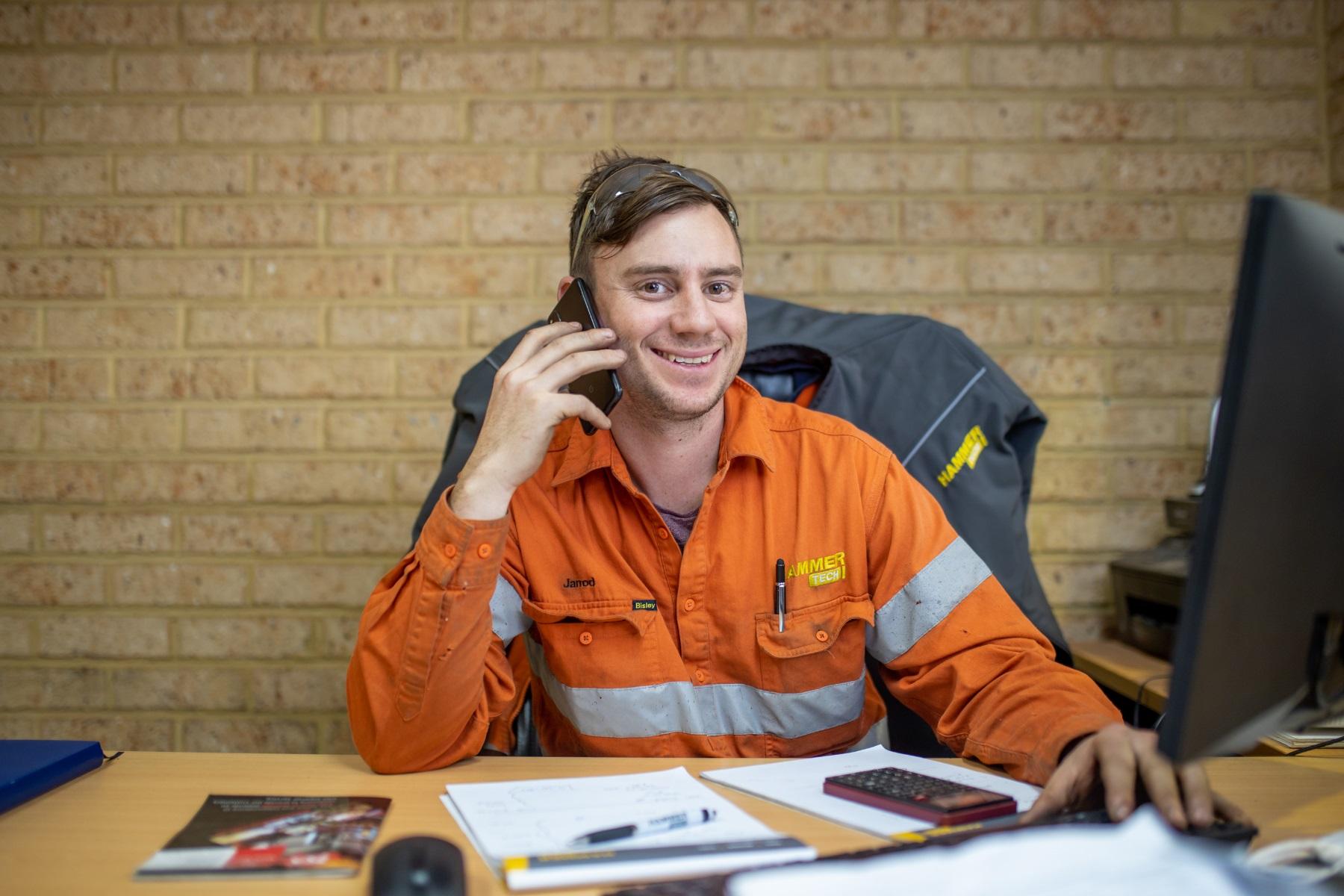 Photo of a man sitting at a desk while talking on the phone.