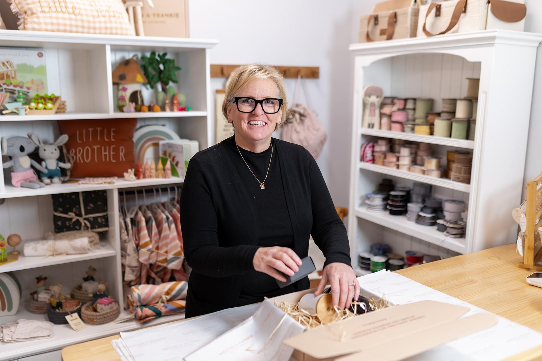 A woman standing in a gift store. She is at the counter, packing a hamper.