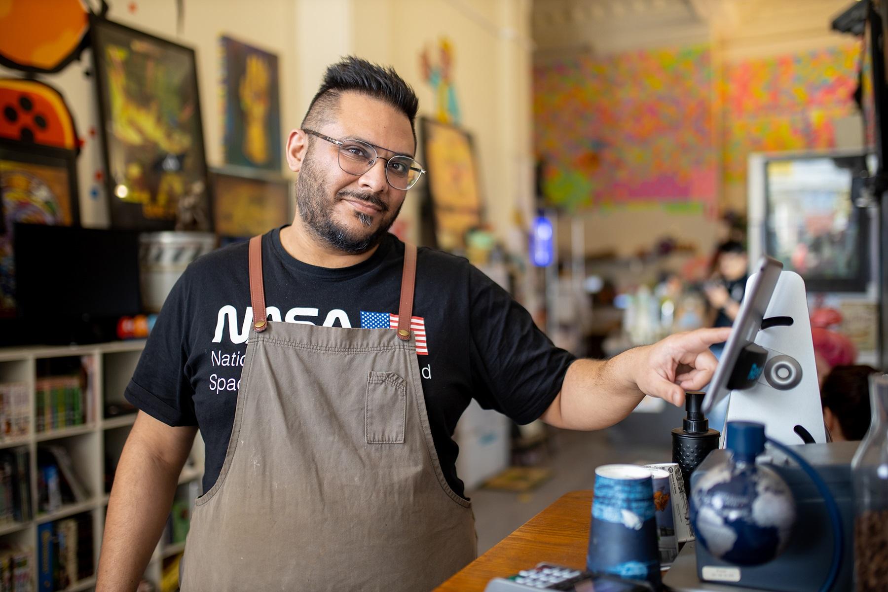 Photo of a male cafe owner. He is inputting an order for a customer using a point of sale terminal.