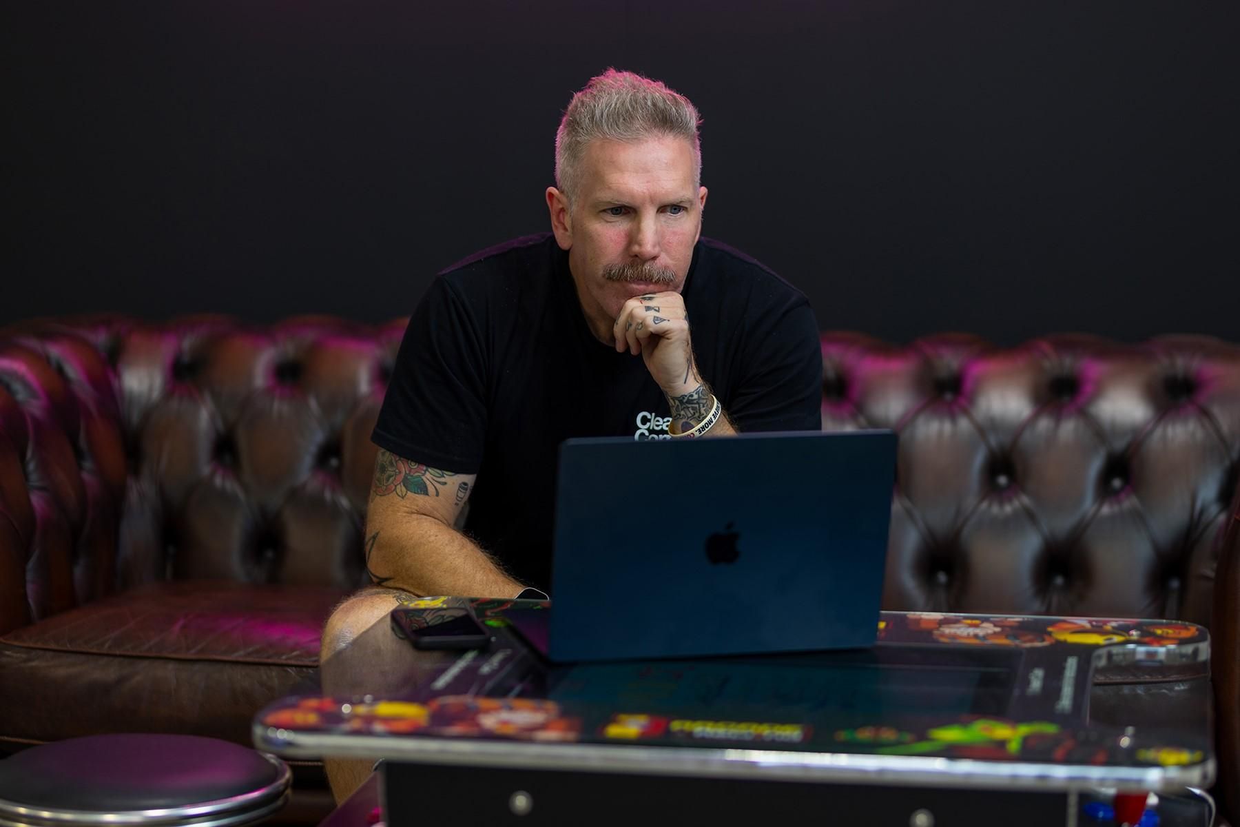 A man sitting on a couch, reading from a laptop.