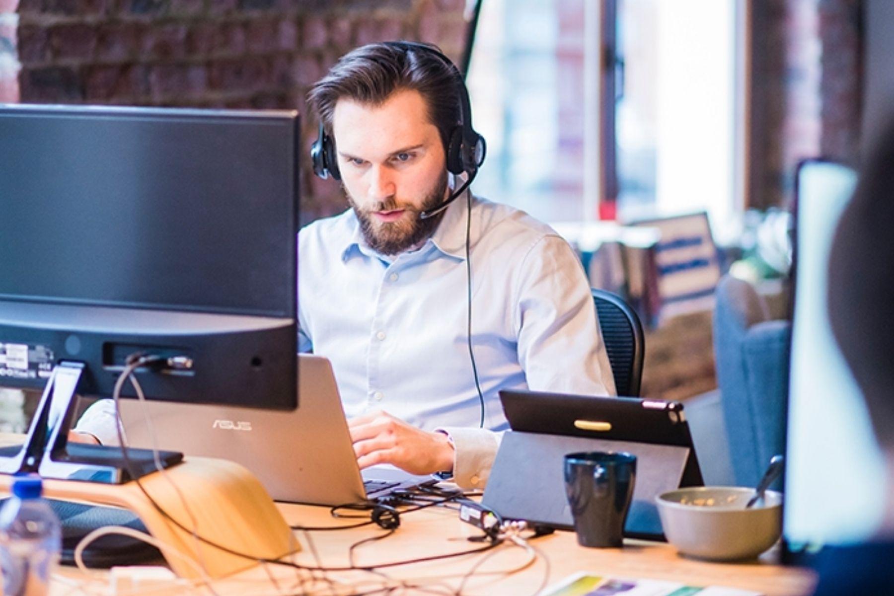 Photo of a man wearing a headset working on a laptop.