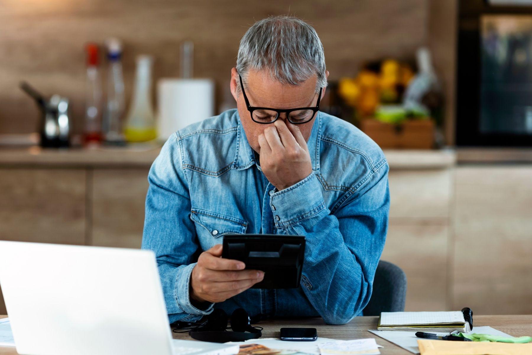 Image of a man on a tablet device in his hand with his head in his other hand.