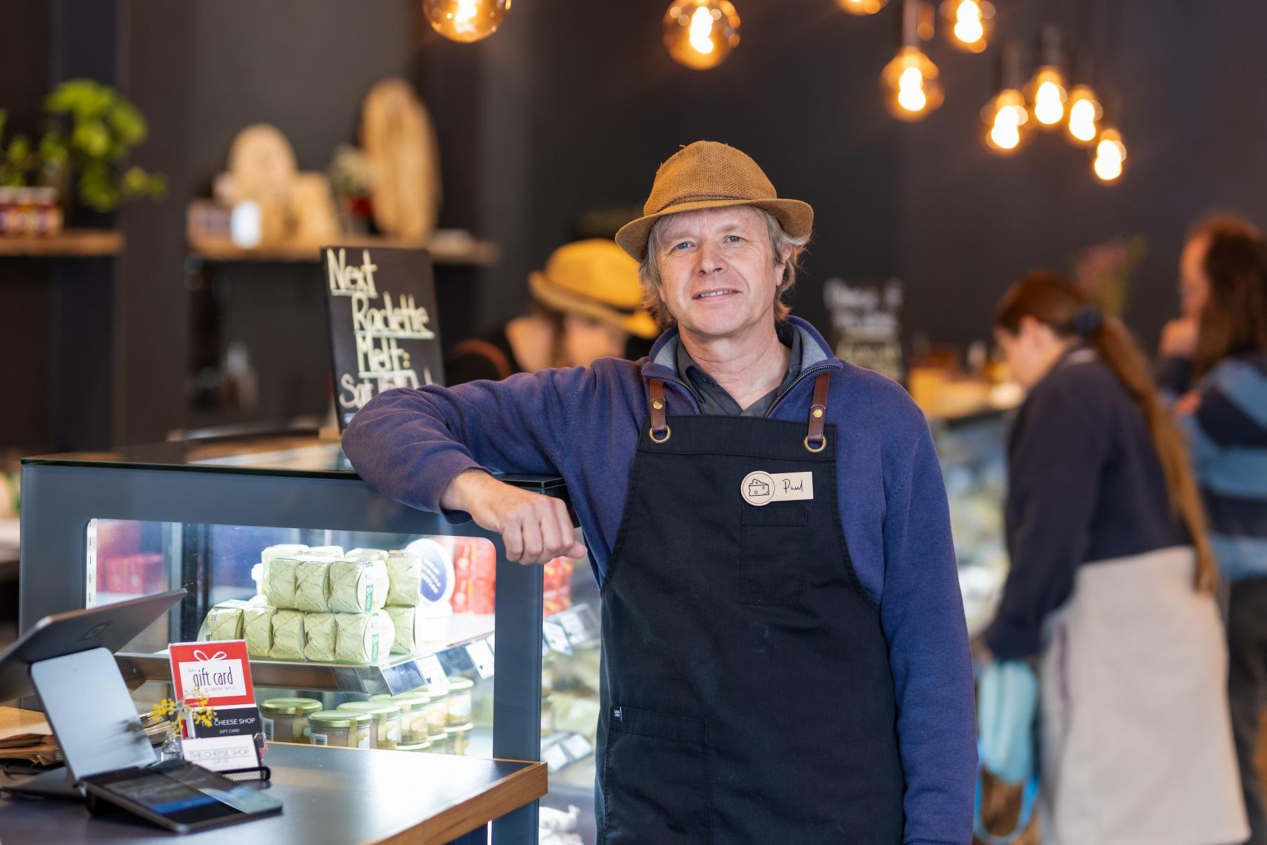 Image of a man in a shop facing the camera with his arm and elbow up on a fresh produce display cabinet