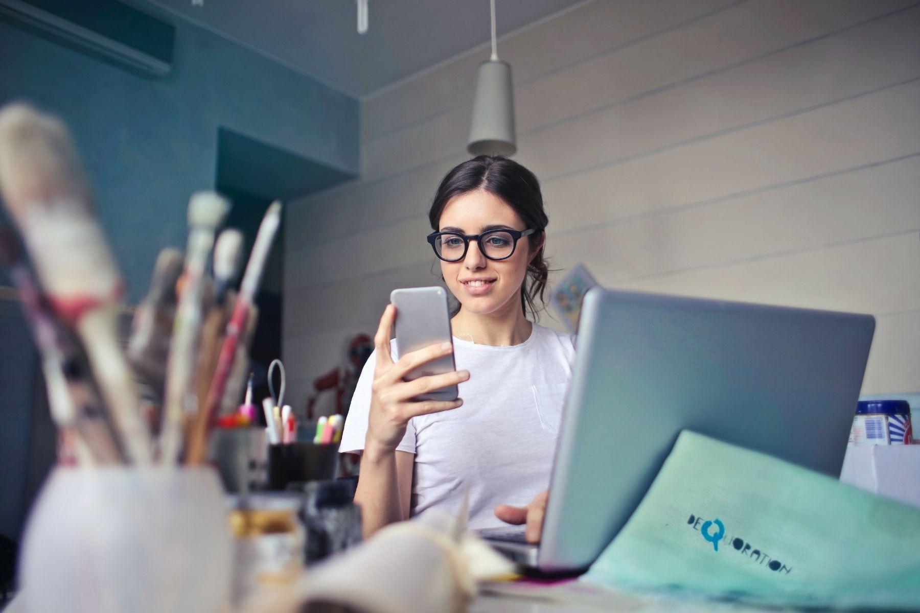 Photo of a woman looking at a smart phone while working in an art studio.