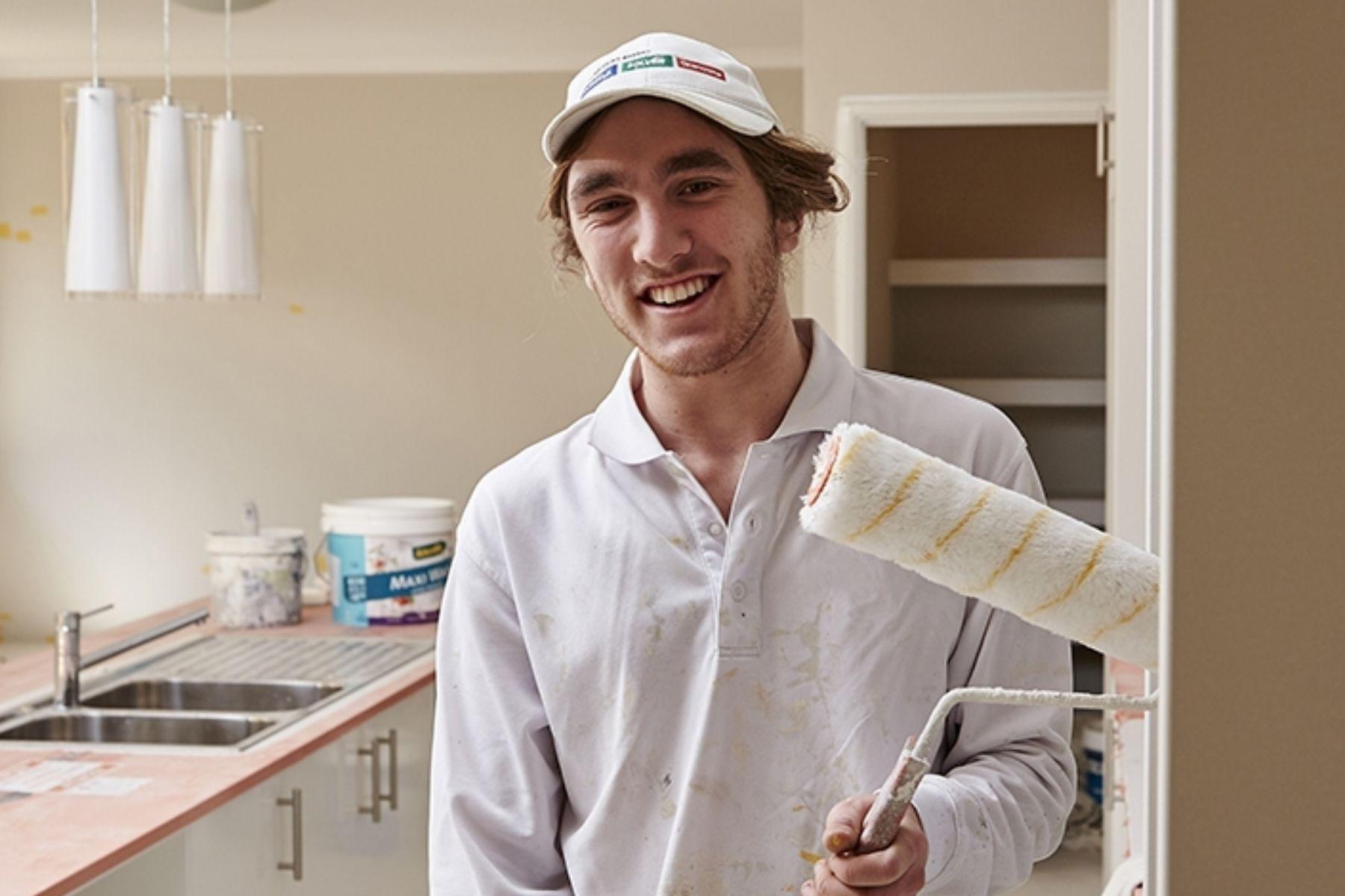 Photo of a house painter in a kitchen holding a paint roller.