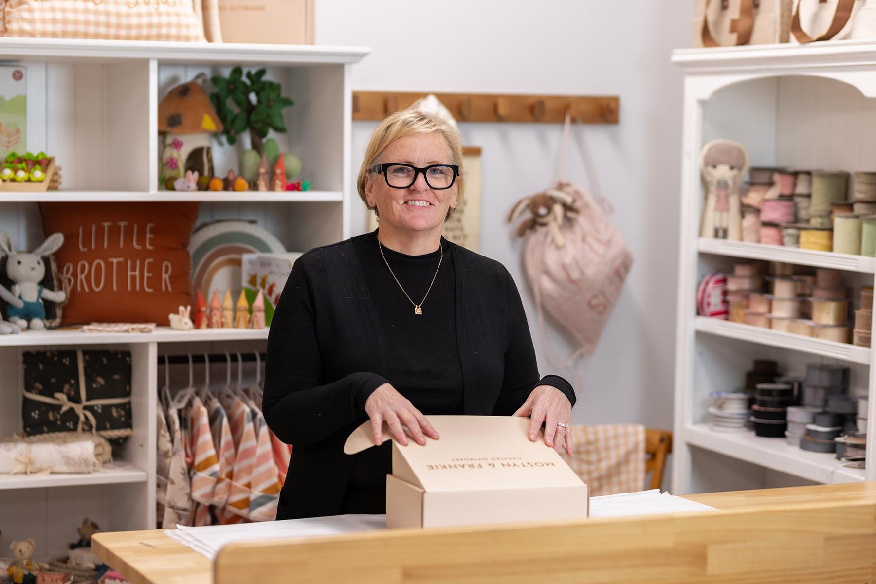 Woman standing behind the counter of her retail store. She has a box of products in front of her on the counter.