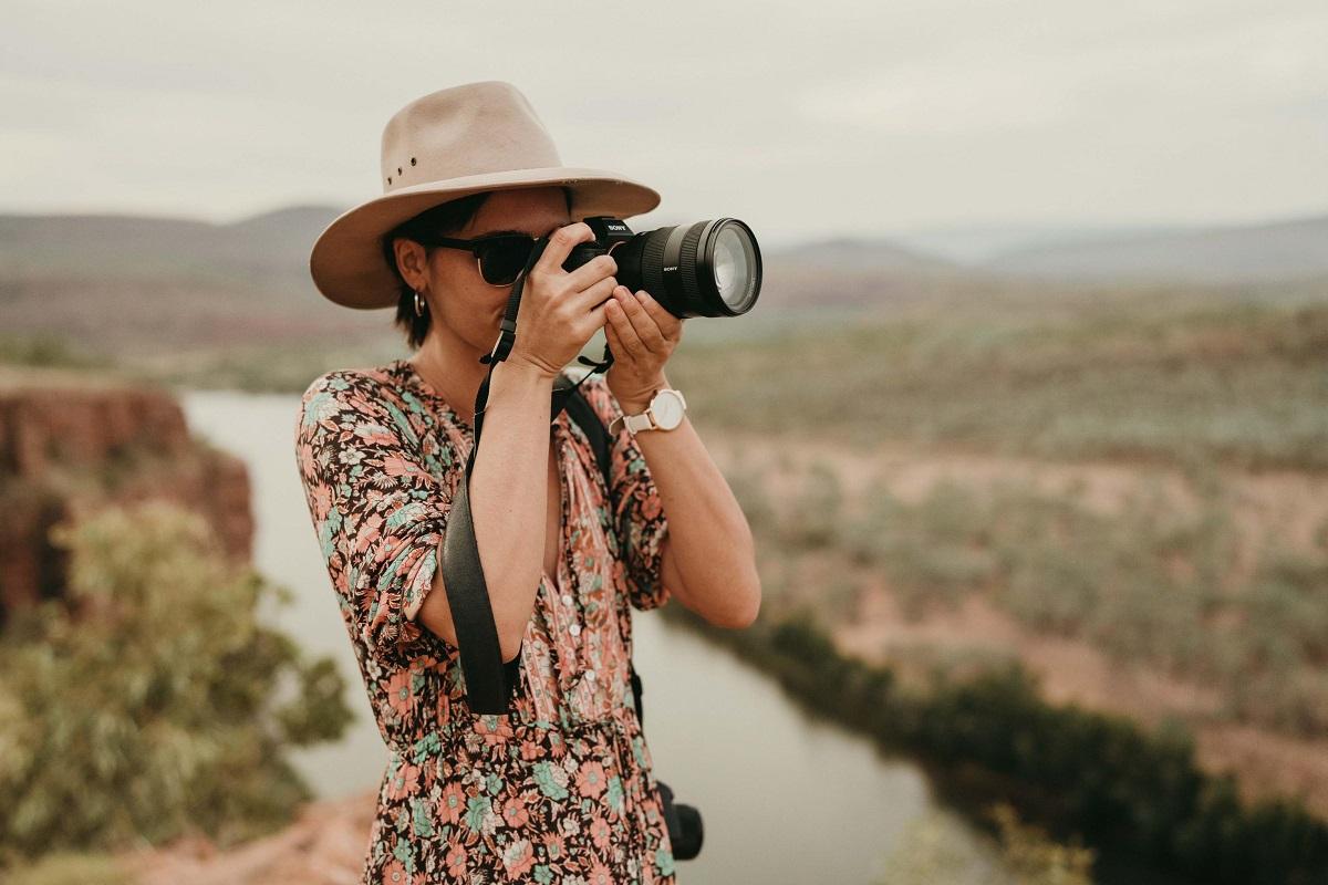 Image of a lady out in the country with a hat on, looking into the lens of a camera
