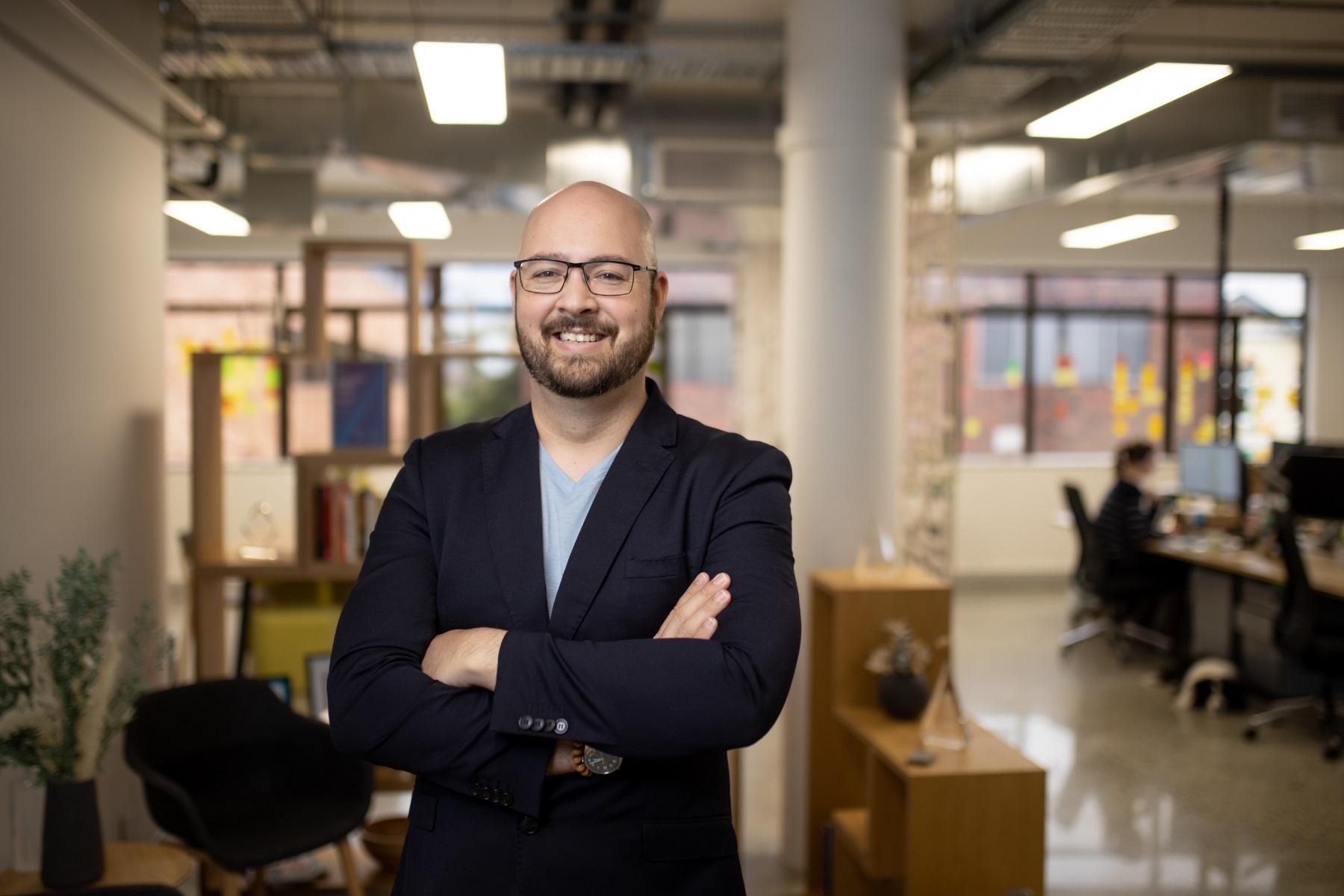 Photo of a man standing in an open floor plan office.