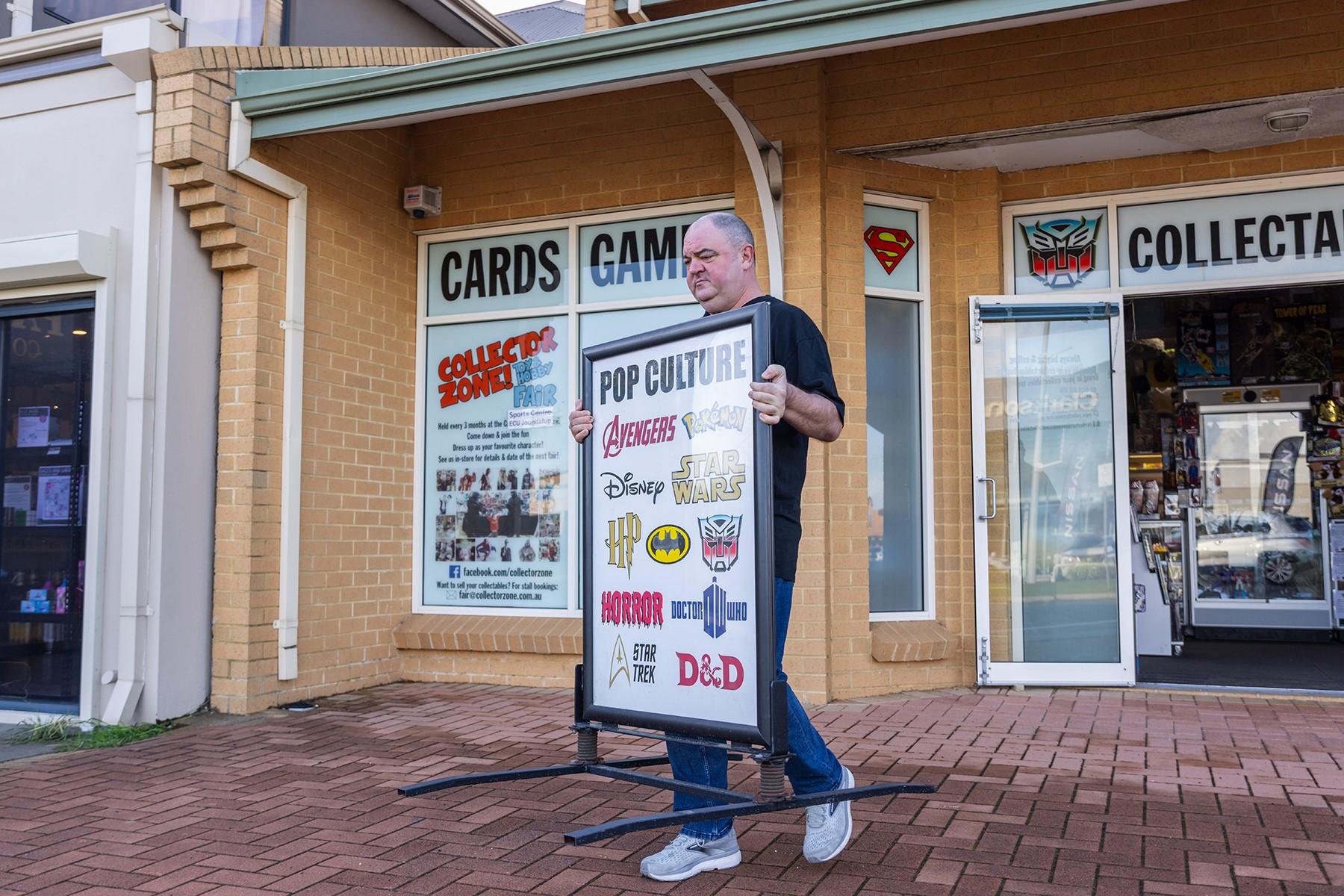 A man carrying a sign out to the front of his business.