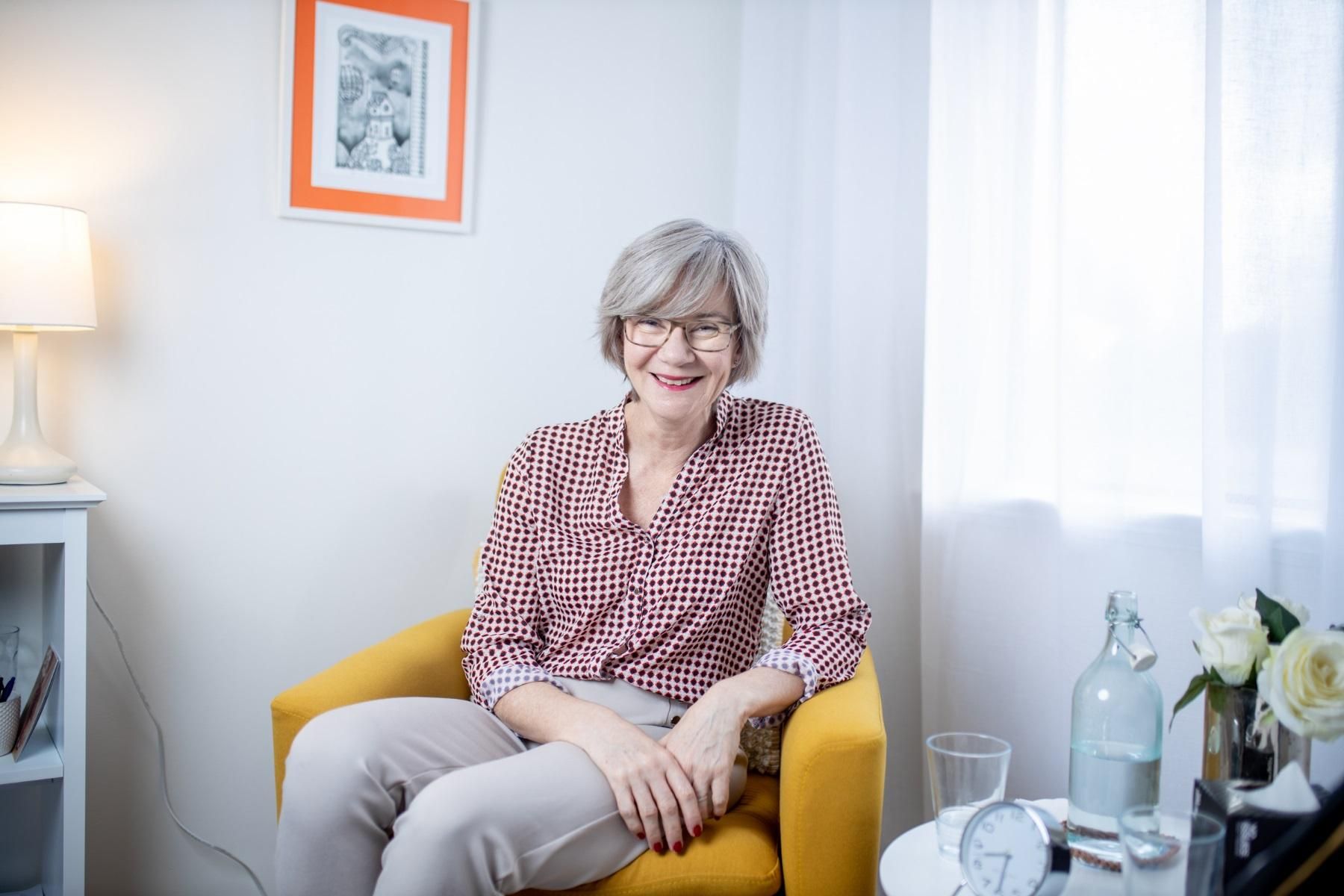 Photo of a woman sitting in an arm chair smiling at the camera.