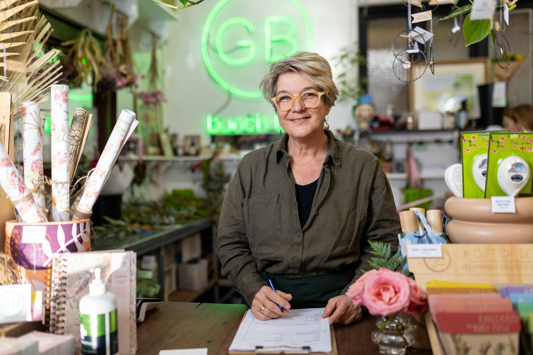 Photo of a female business owner. She is standing behind the counter of her florist business.