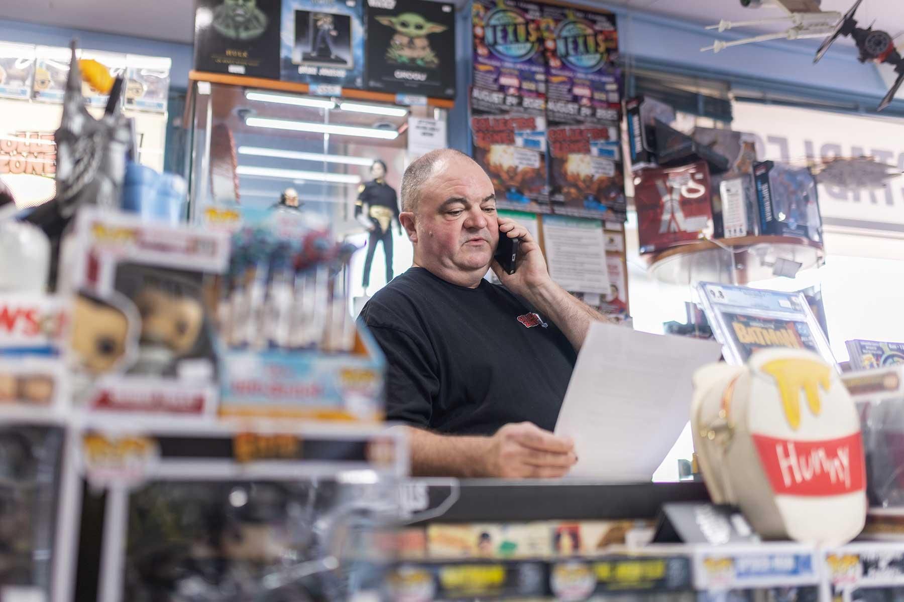 Man on the phone working behind the counter at Collector Zone shop in Perth.