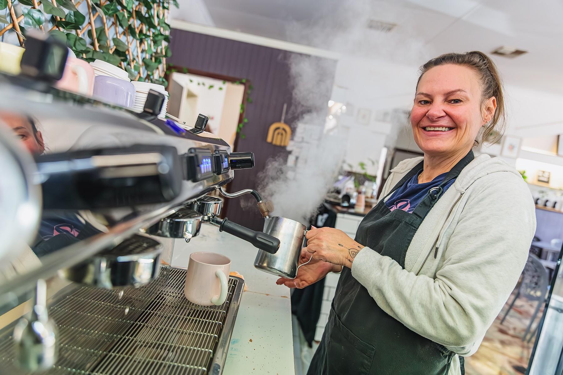 A woman standing at a coffee machine. She is smiling at the camera.