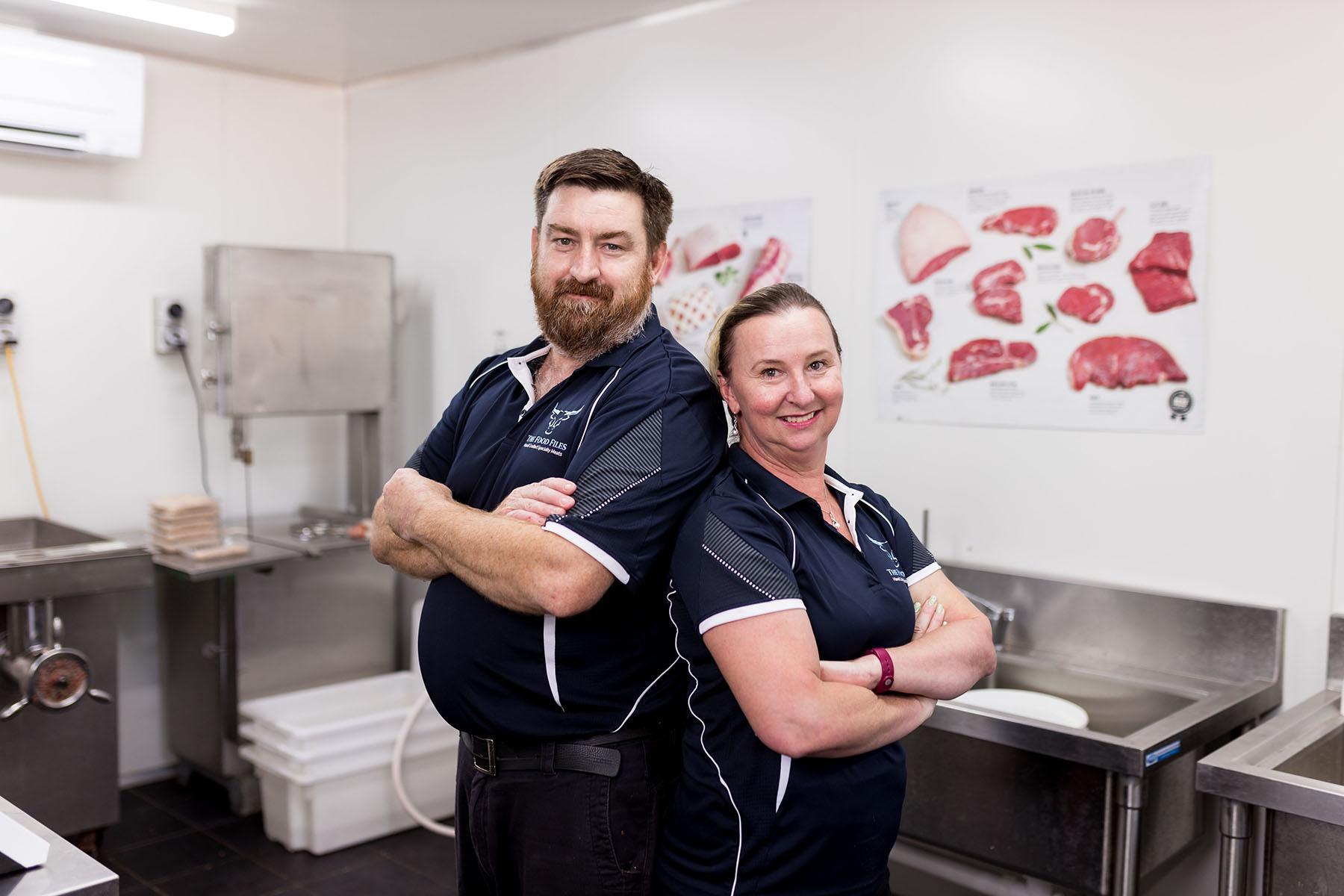 Photo of a man and woman standing back to back in their butcher shop, which is located in regional Western Australia.
