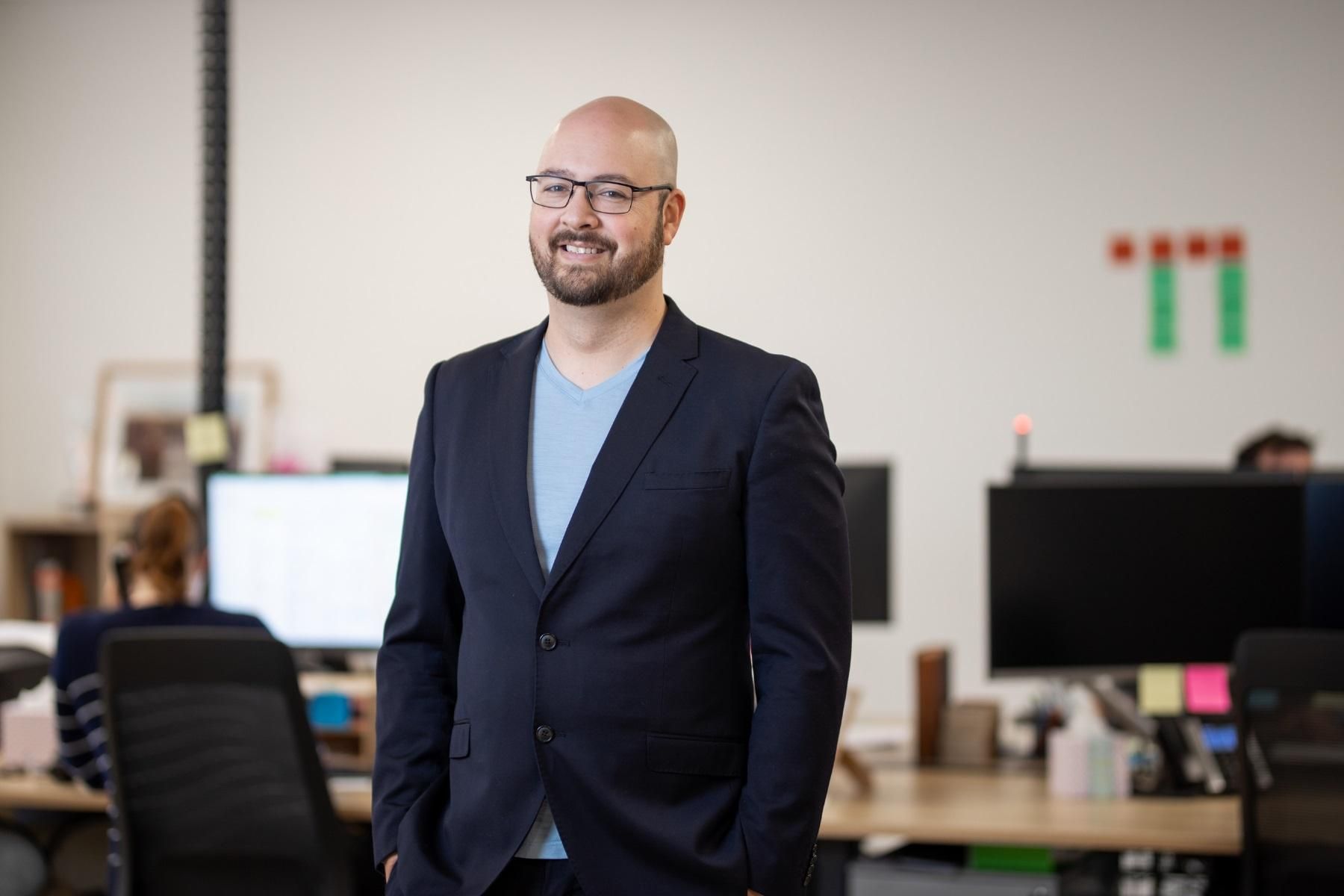 Photo of a man standing in an office looking towards the camera.