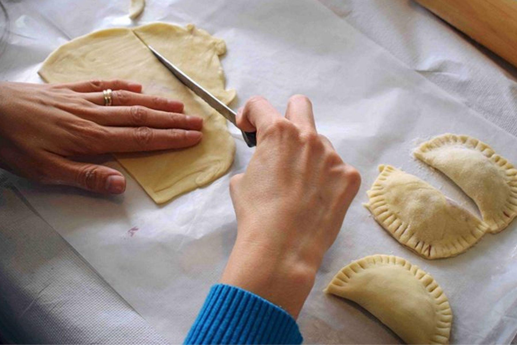 Close up photo of a woman's hands cutting pastry with a knife.