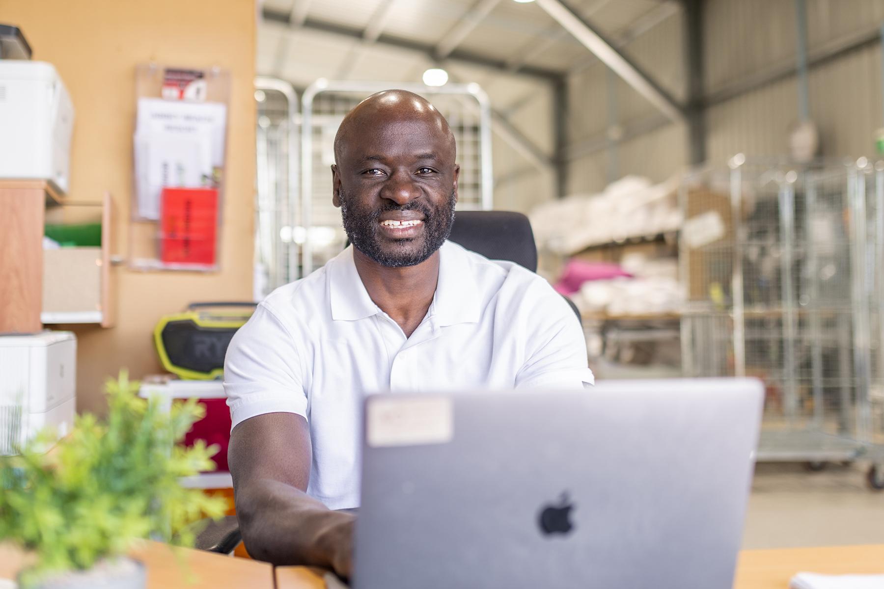 Photo of a man sitting at a desk in his laundry business. He is working on a laptop.