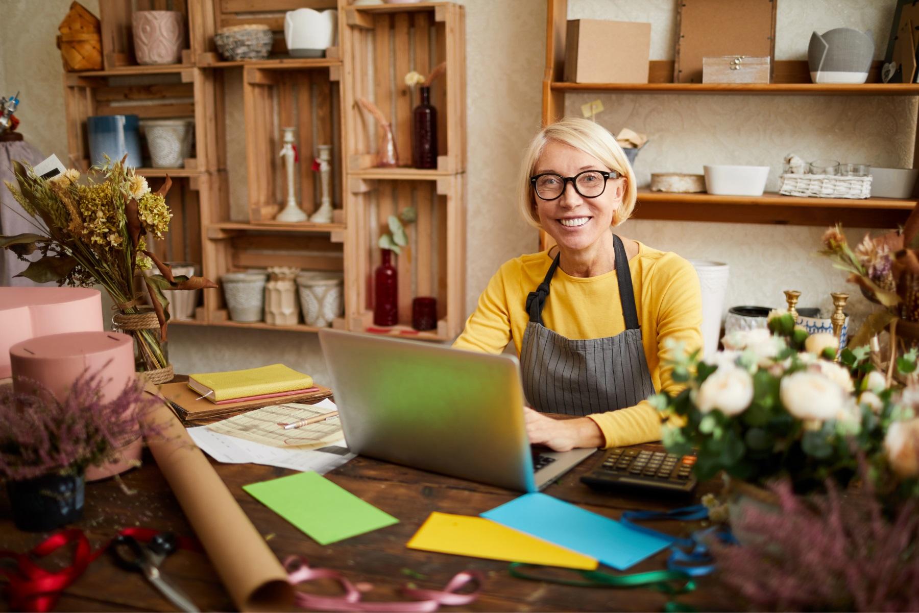 Photo of a woman sitting at a table in a florist business typing on a laptop.