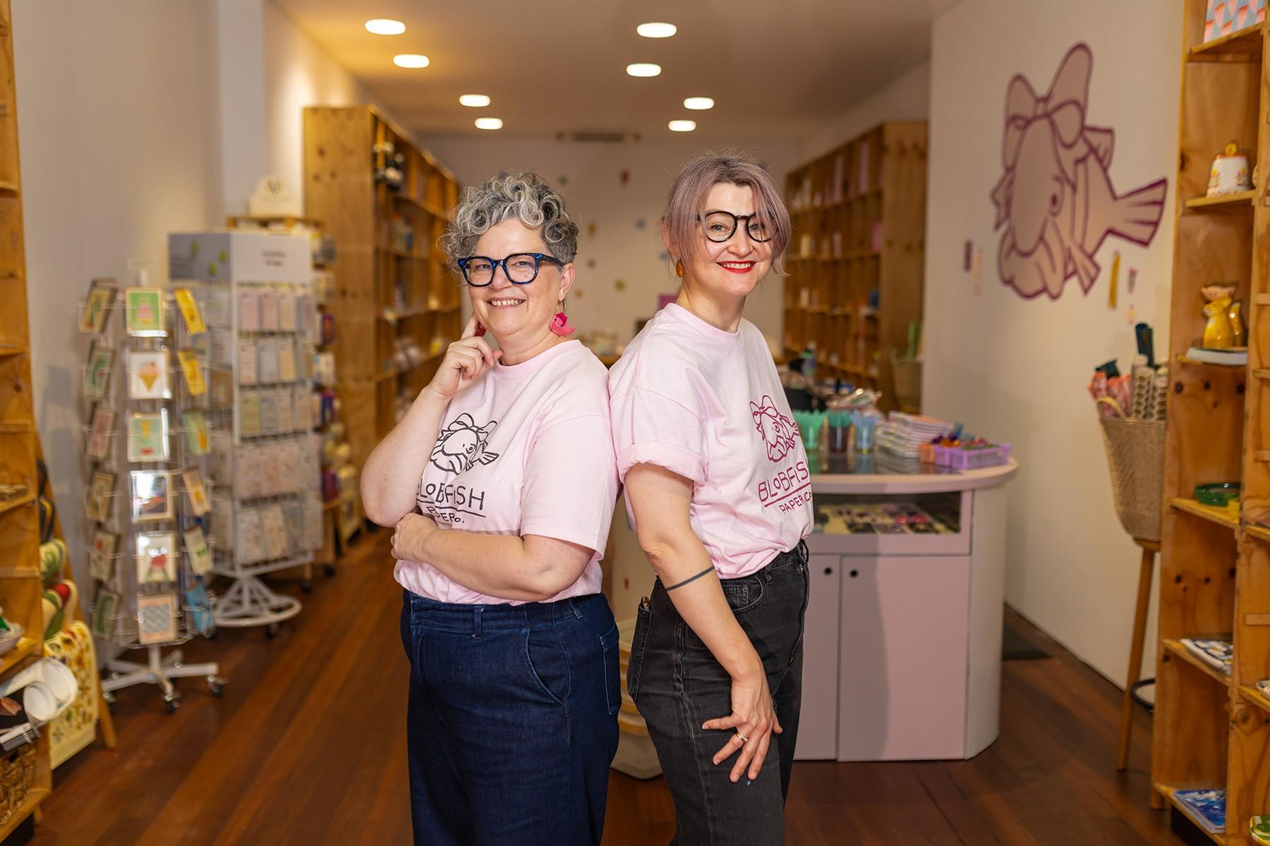Two female business owners standing back to back in their business premises.