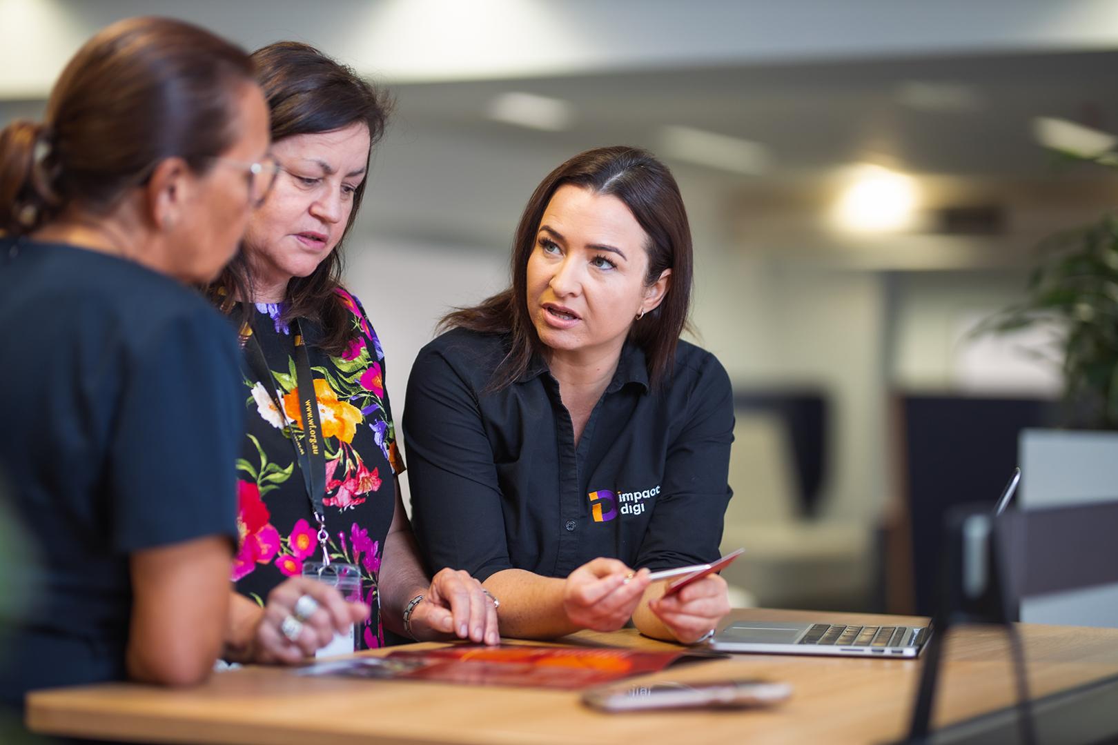 Image of three women leaning over a desk talking