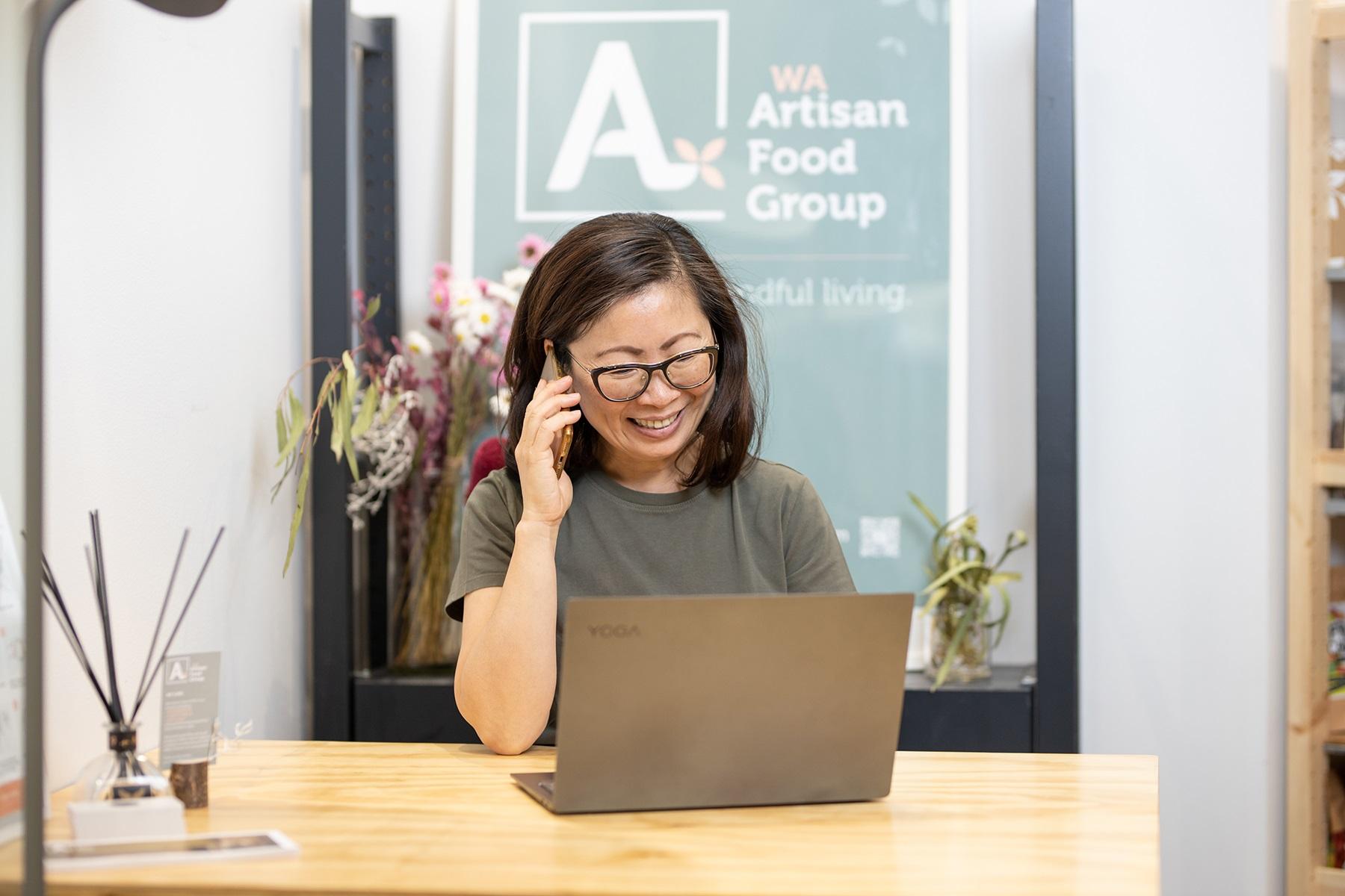 Photo of a woman sitting in front of a laptop. She is talking on the phone and smiling.