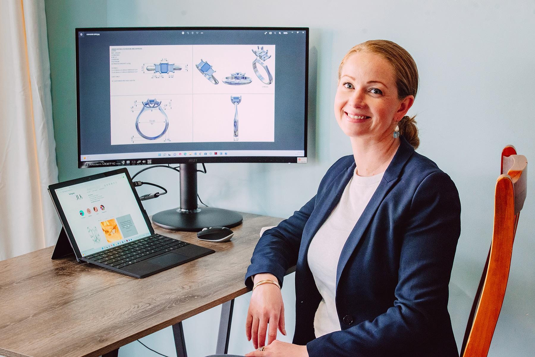 Photo of Julianne Karavitis. She is sitting at a desk with a computer and smiling at the camera.