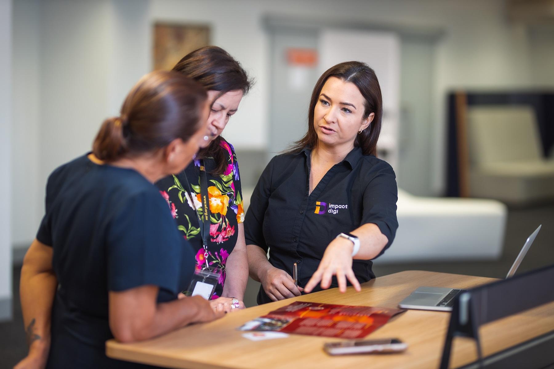 Photo of a female business owner explaining a product to two female customers. They are in an office setting.