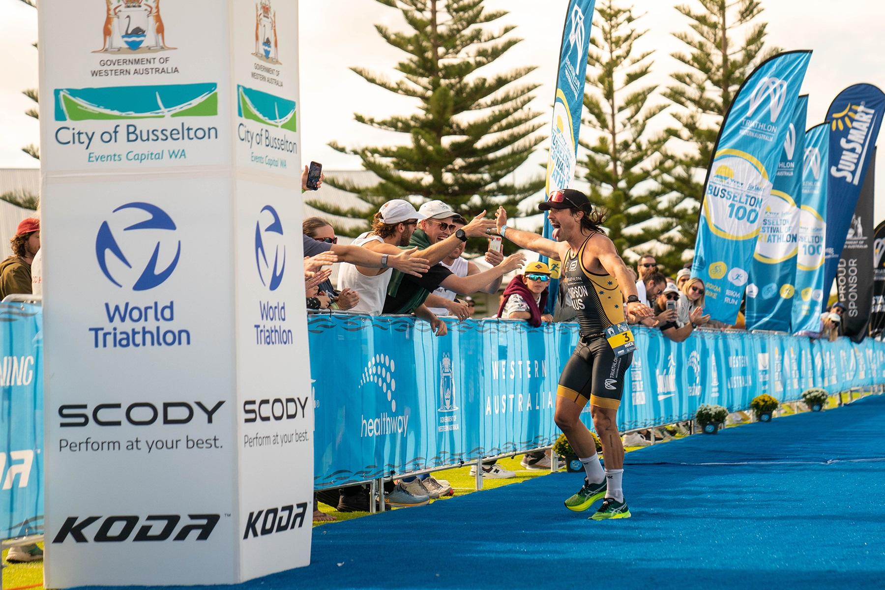 Photo of a man competing in a triathlon event in Bunbury. He is high fiving spectators as he heads towards the finish line.