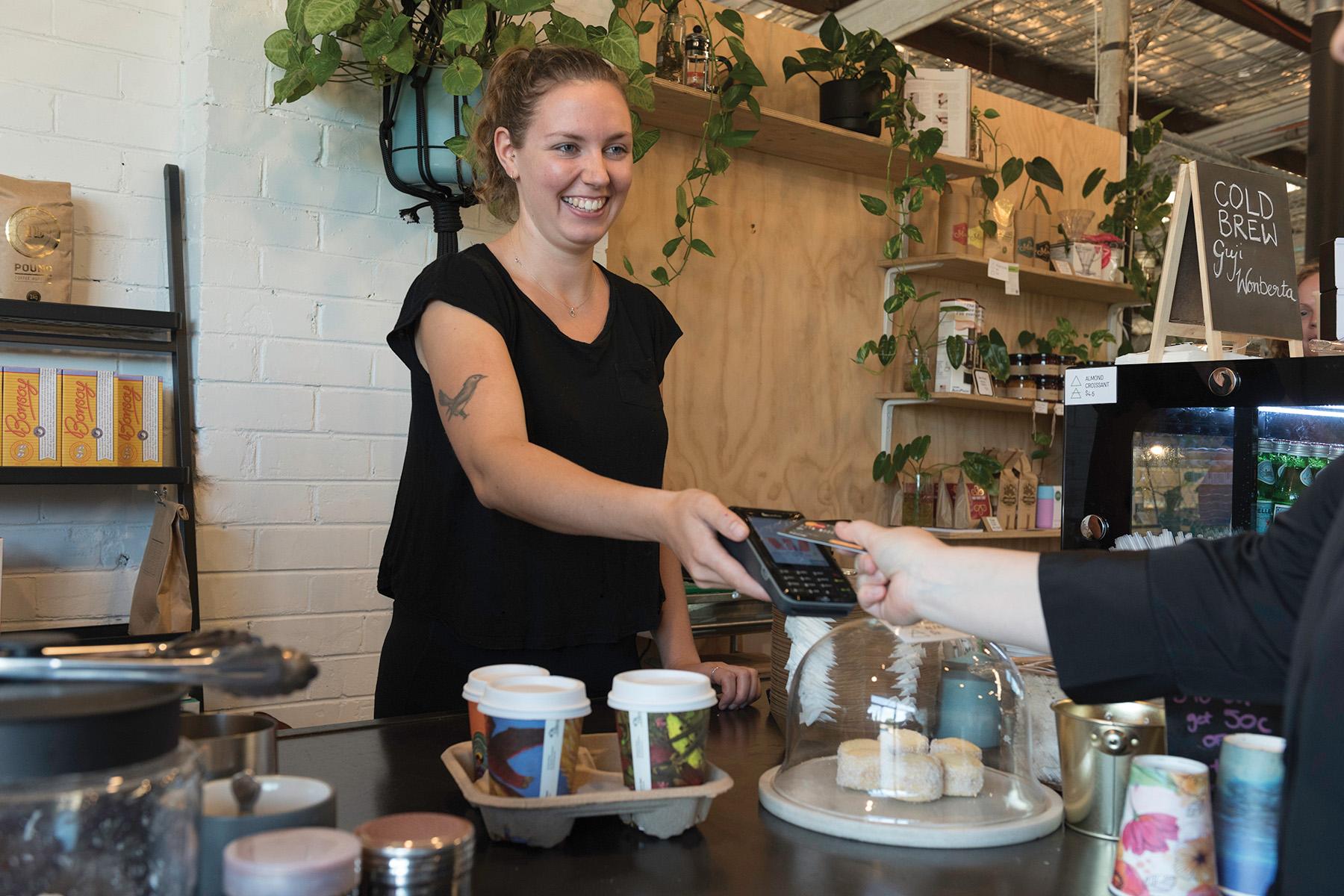 Photo of a female cafe owner accepting a payment via bank card from a customer.